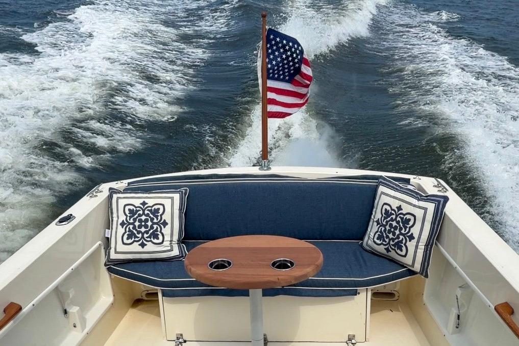 2006 Atlas Boat Works Acadia 25 with American flag, blue seating, and decorative pillows.