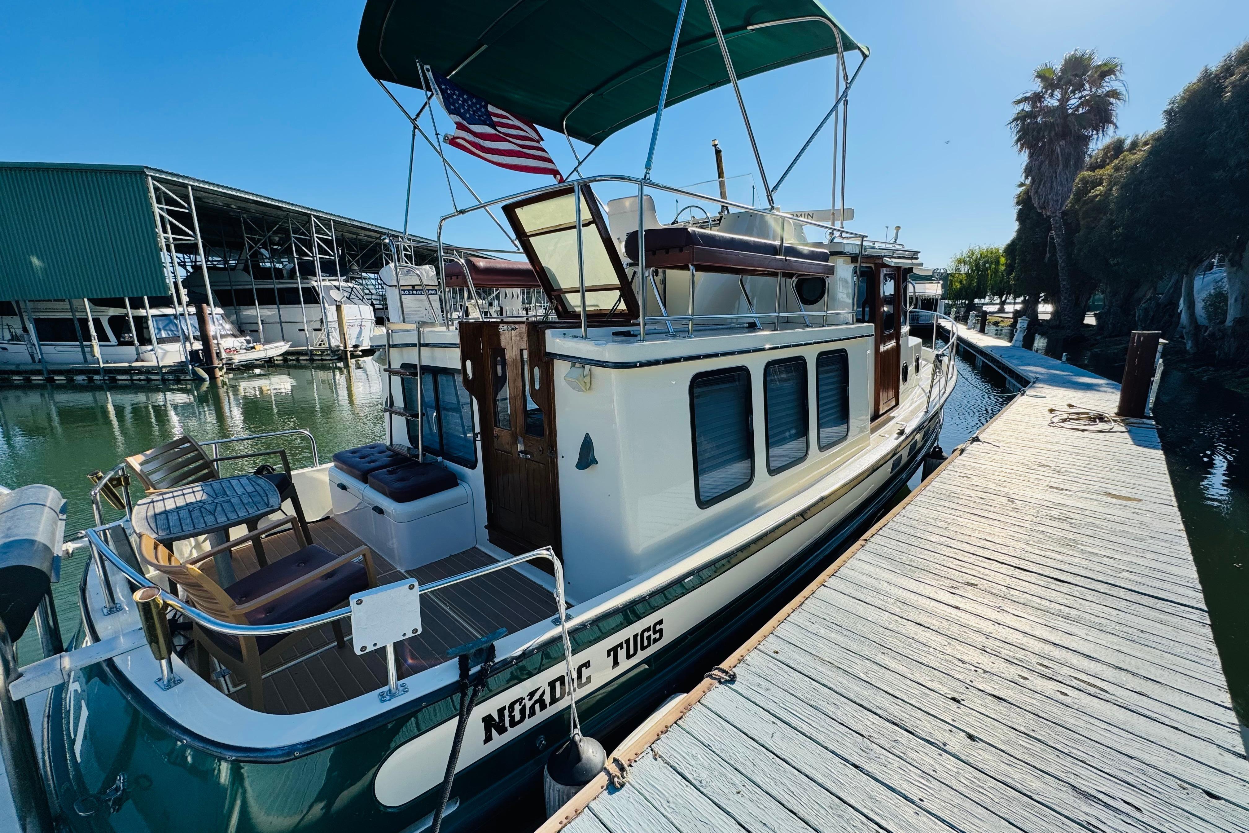 1996 Nordic Tug 32 docked, featuring classic design and American flag, under sunny skies.