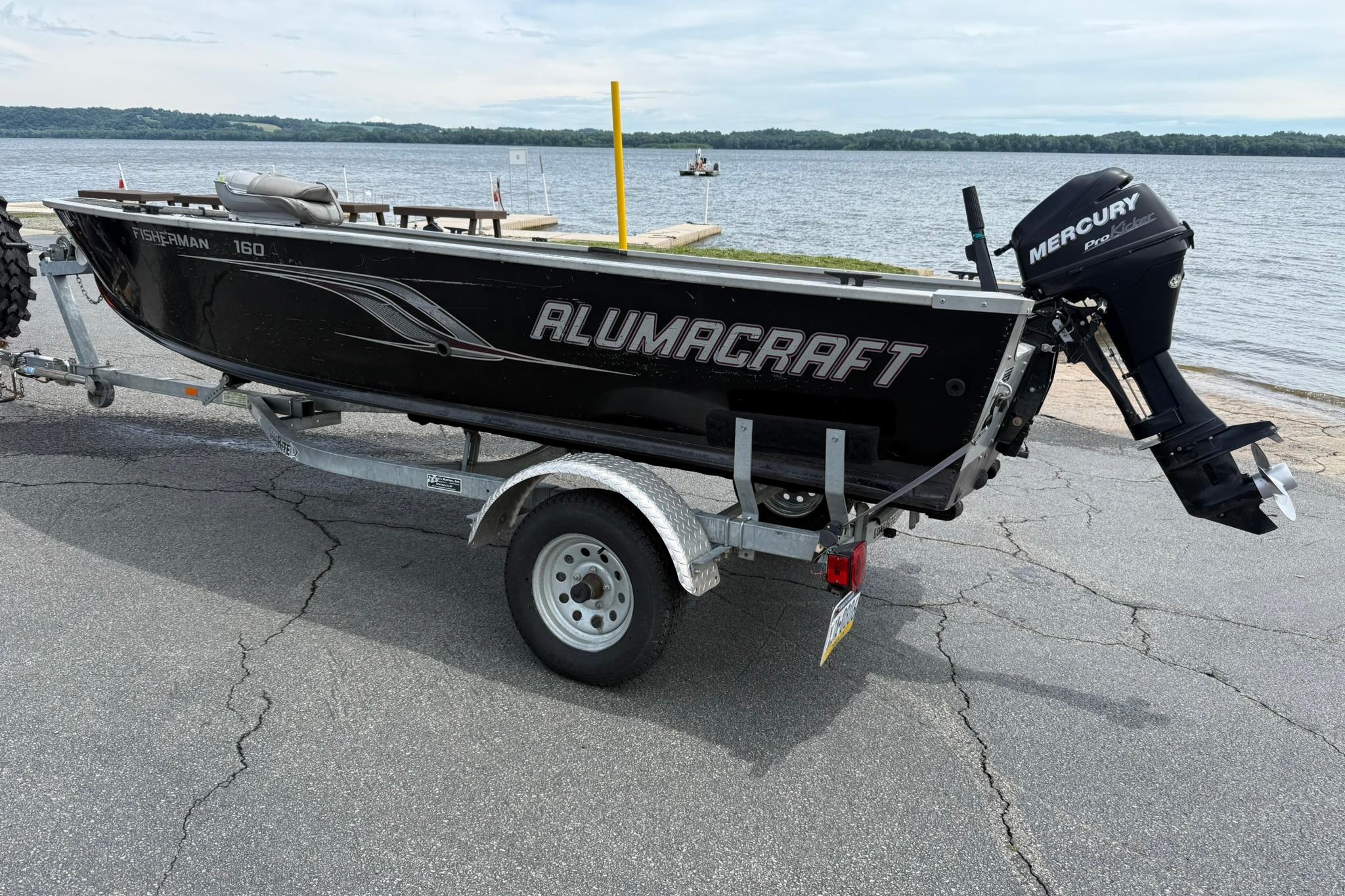 2013 Alumacraft Fisherman 160 Tiller boat on trailer by a lake.