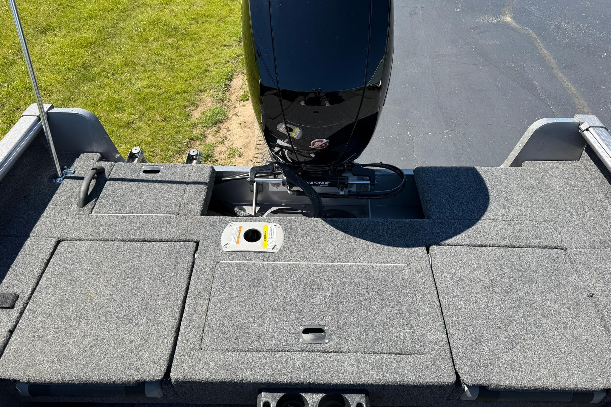 2024 Lund 1875 Impact XS Sport boat deck with motor, featuring carpeted storage compartments.