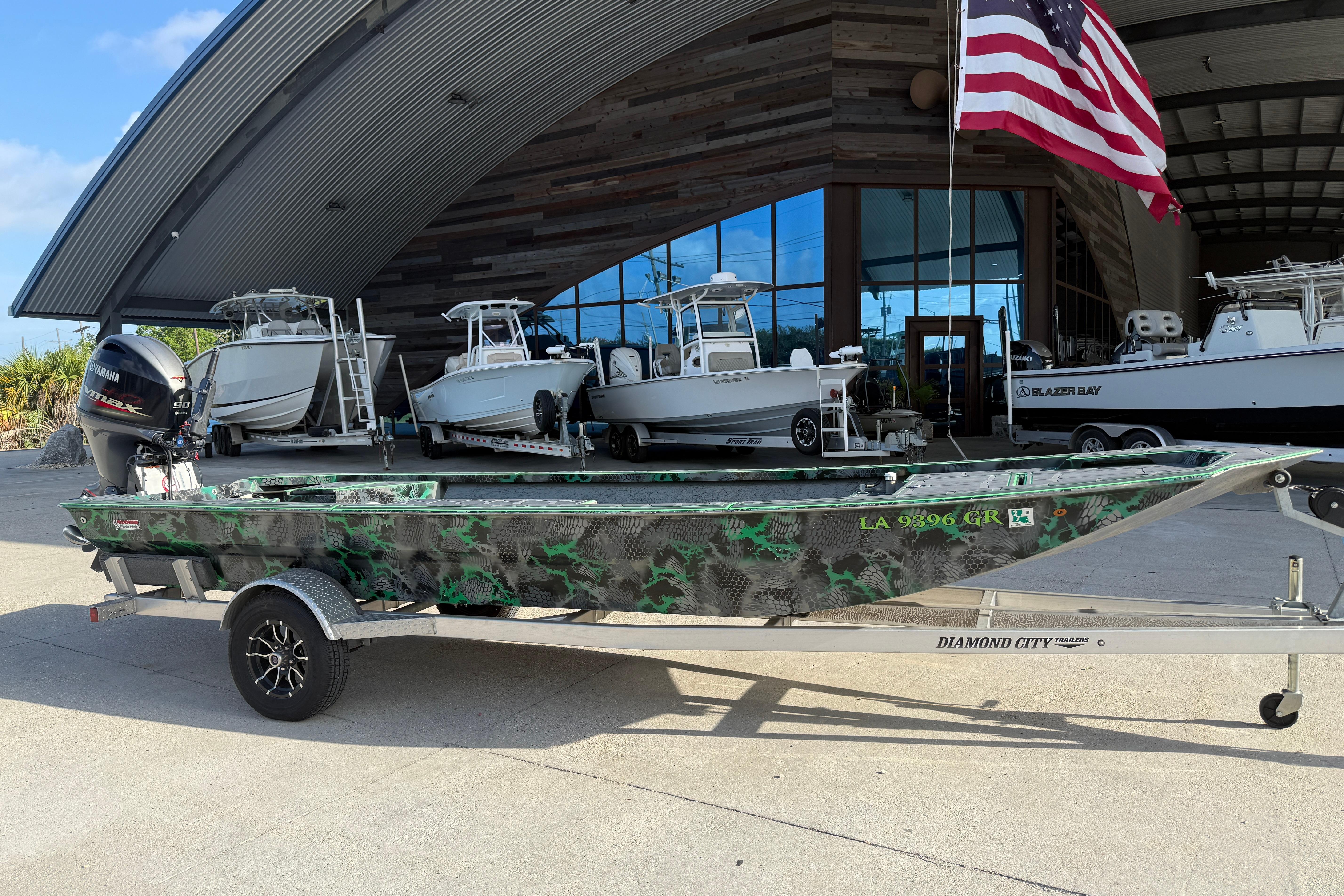 Custom Rene Gros 20x48 boat, 2024 model, on trailer outside a showroom with American flag.