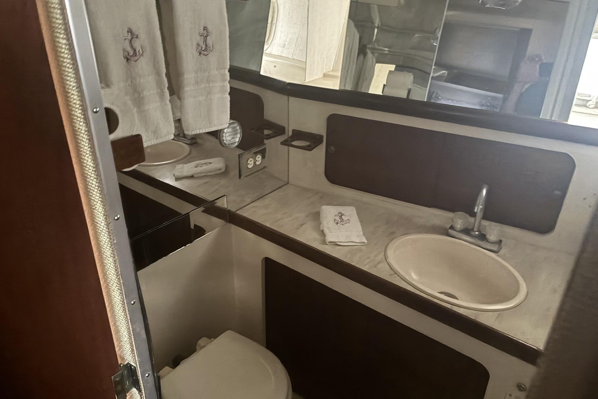 1980 Chris-Craft 360 Commander bathroom with sink, mirror, and nautical-themed towels.