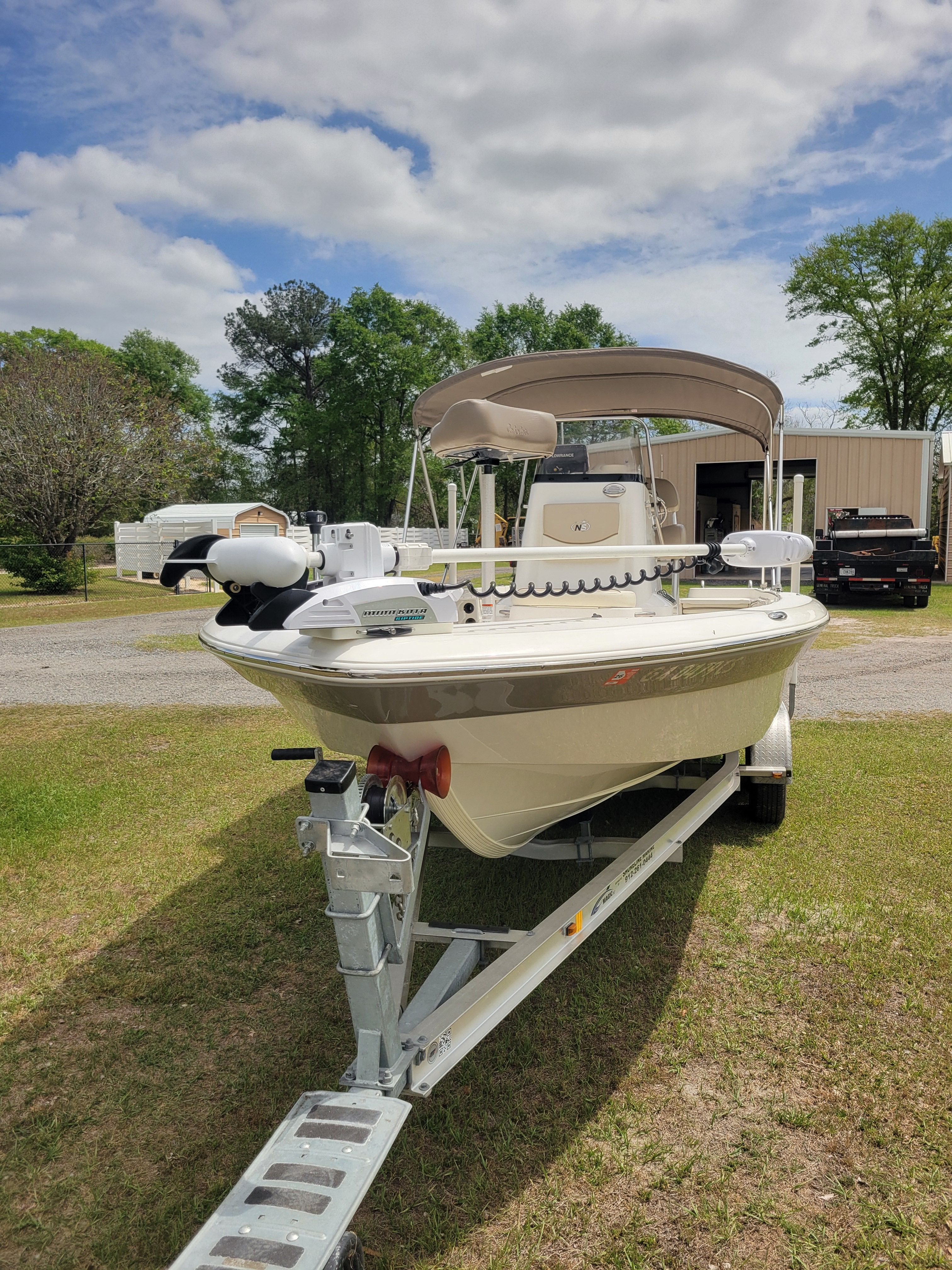 A NauticStar 2200 Sport boat on a trailer, surrounded by trees and vehicles.