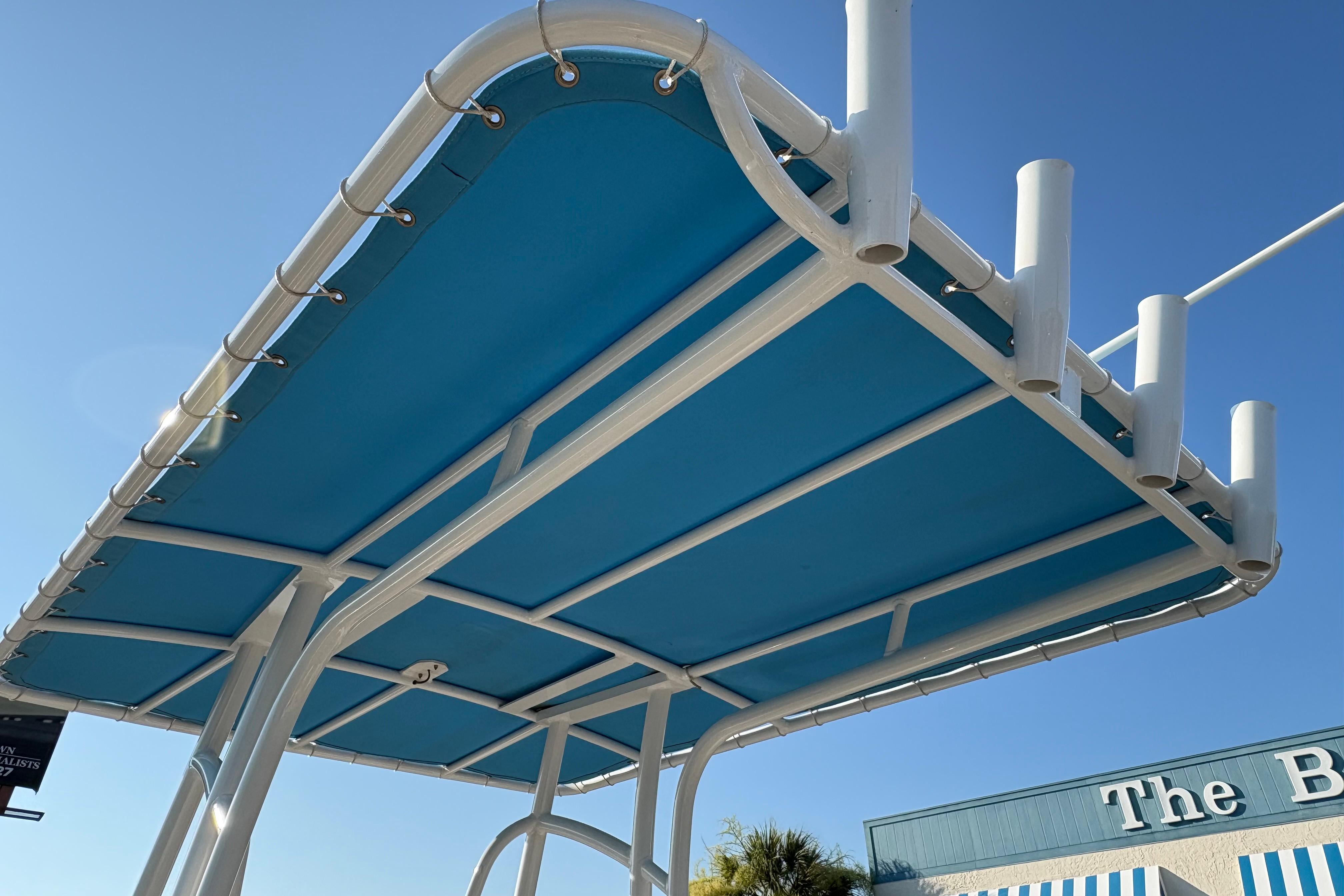 2019 NauticStar 231 Hybrid boat canopy with rod holders against clear blue sky.