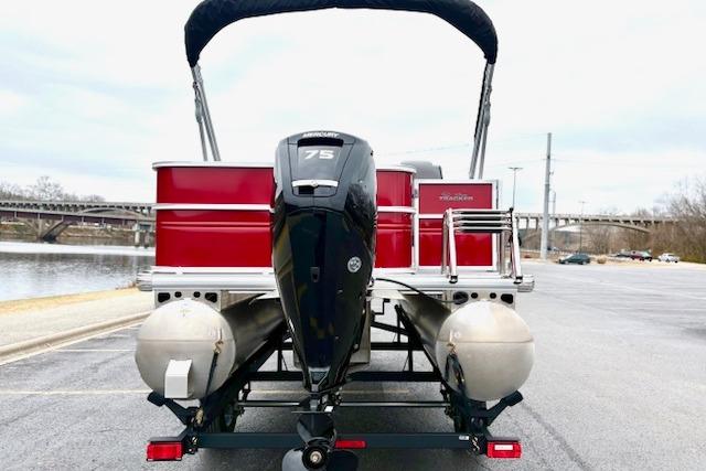 2026 Sun Tracker Party Barge 18 DLX pontoon boat with 75 HP engine, parked by a river.