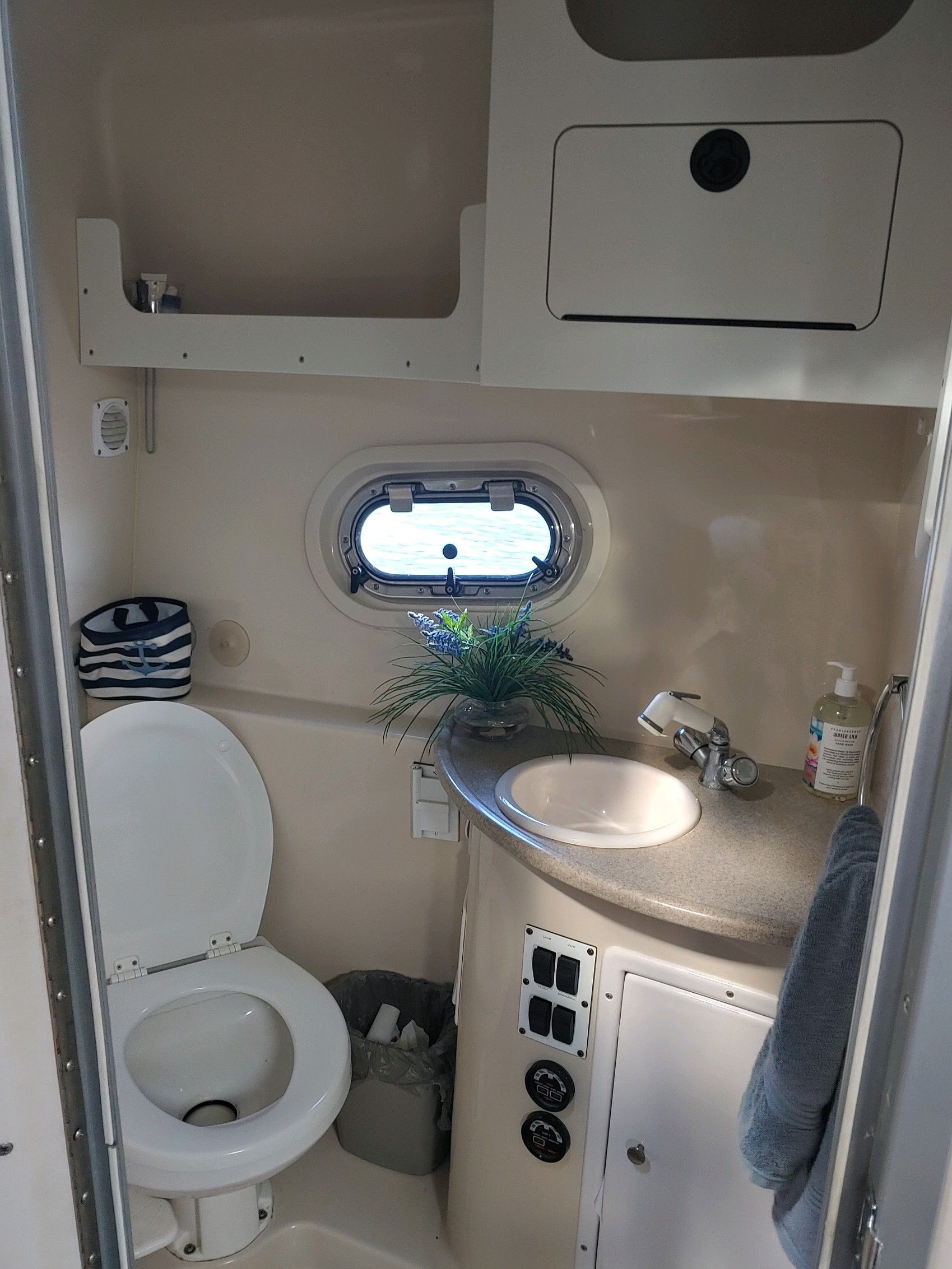 A boat bathroom with a toilet, sink, and small window.