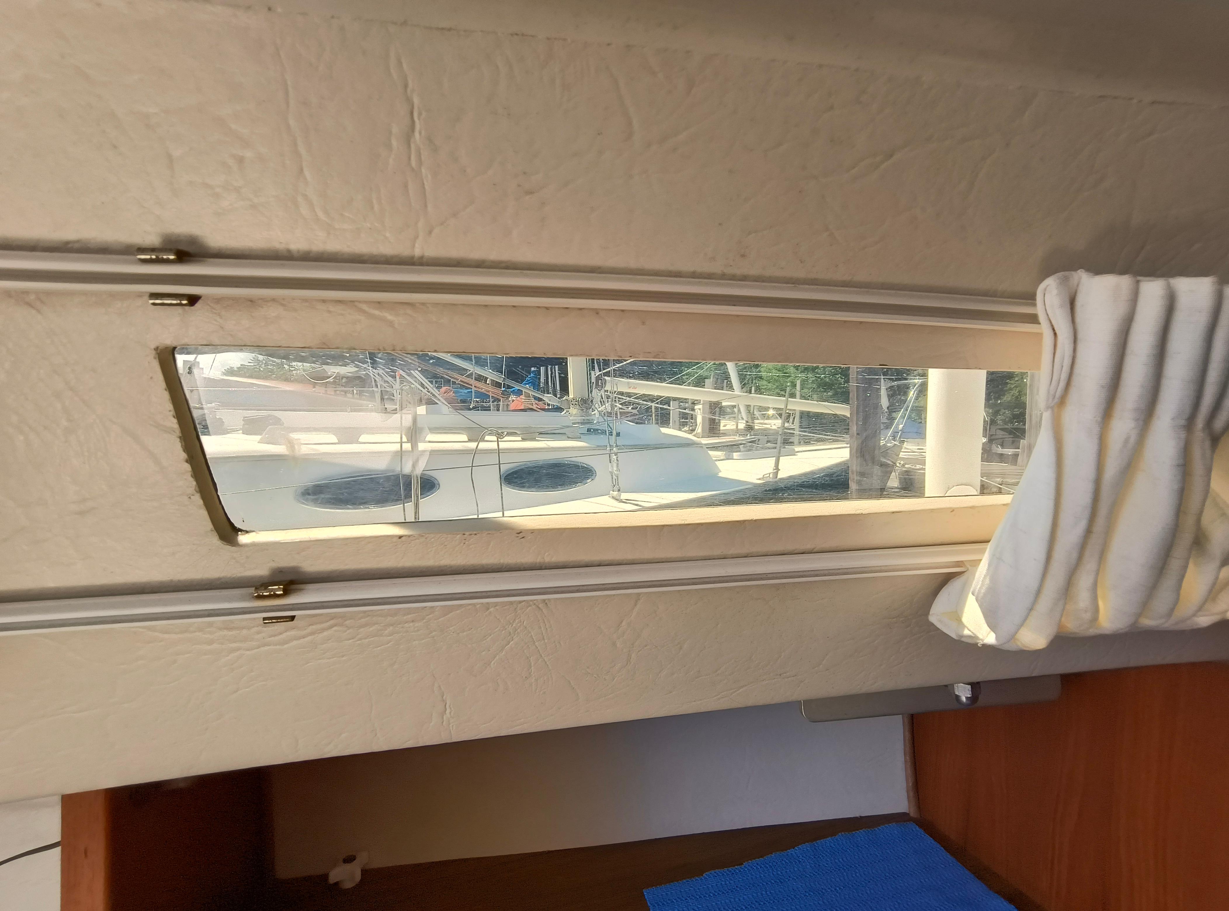 Interior view of a 1985 Catalina 27 sailboat, showing a window with a docked boat outside.
