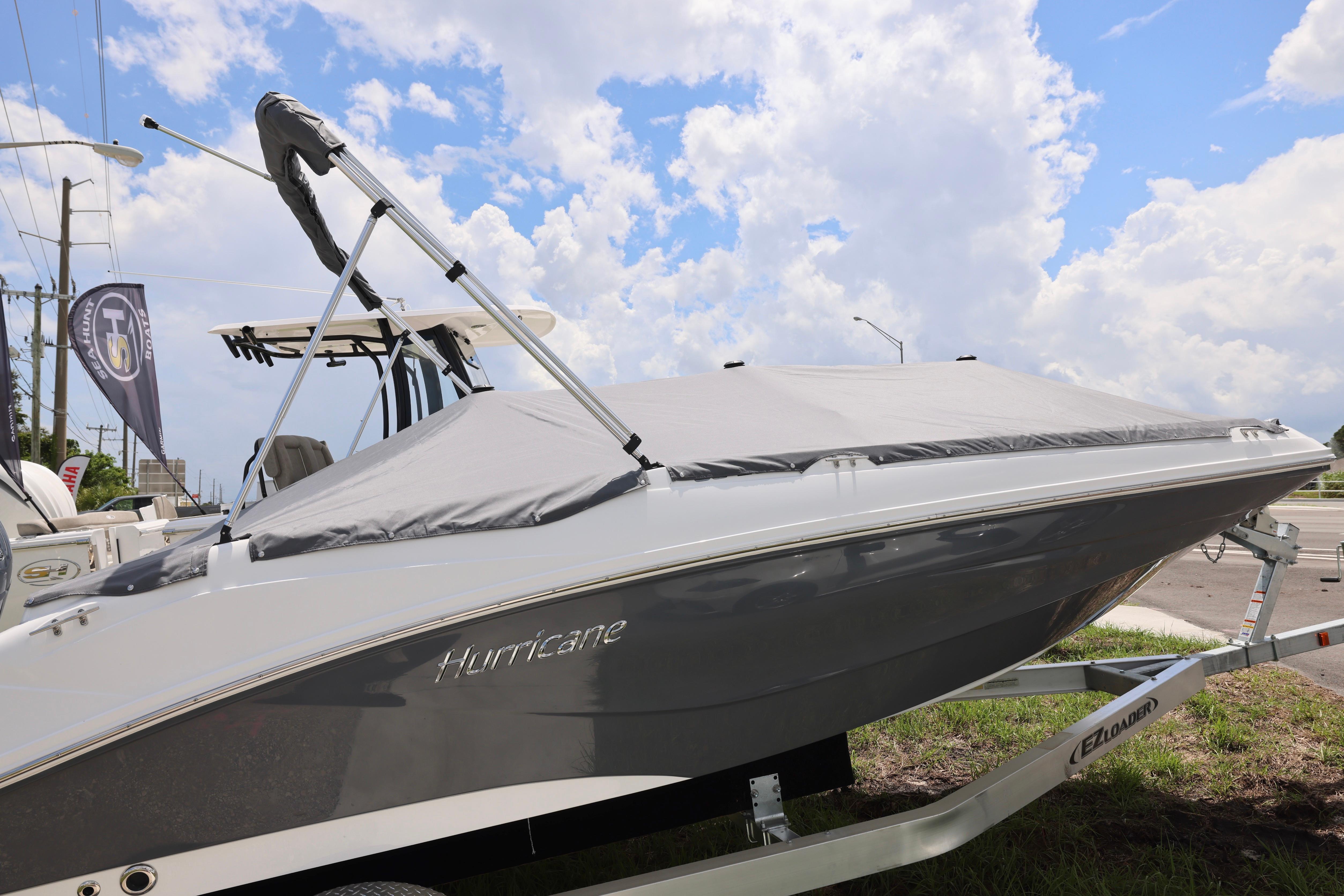 2026 Hurricane SunDeck Sport 205 OB boat with cover on trailer, under a partly cloudy sky.