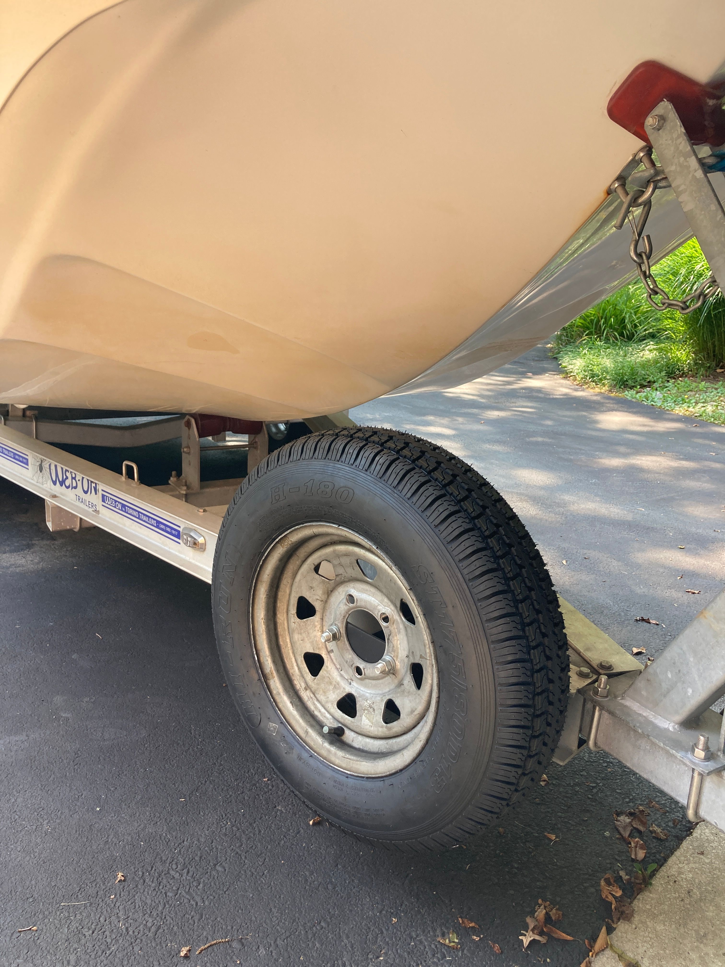 A boat on a trailer with a large tire, parked on a paved surface.