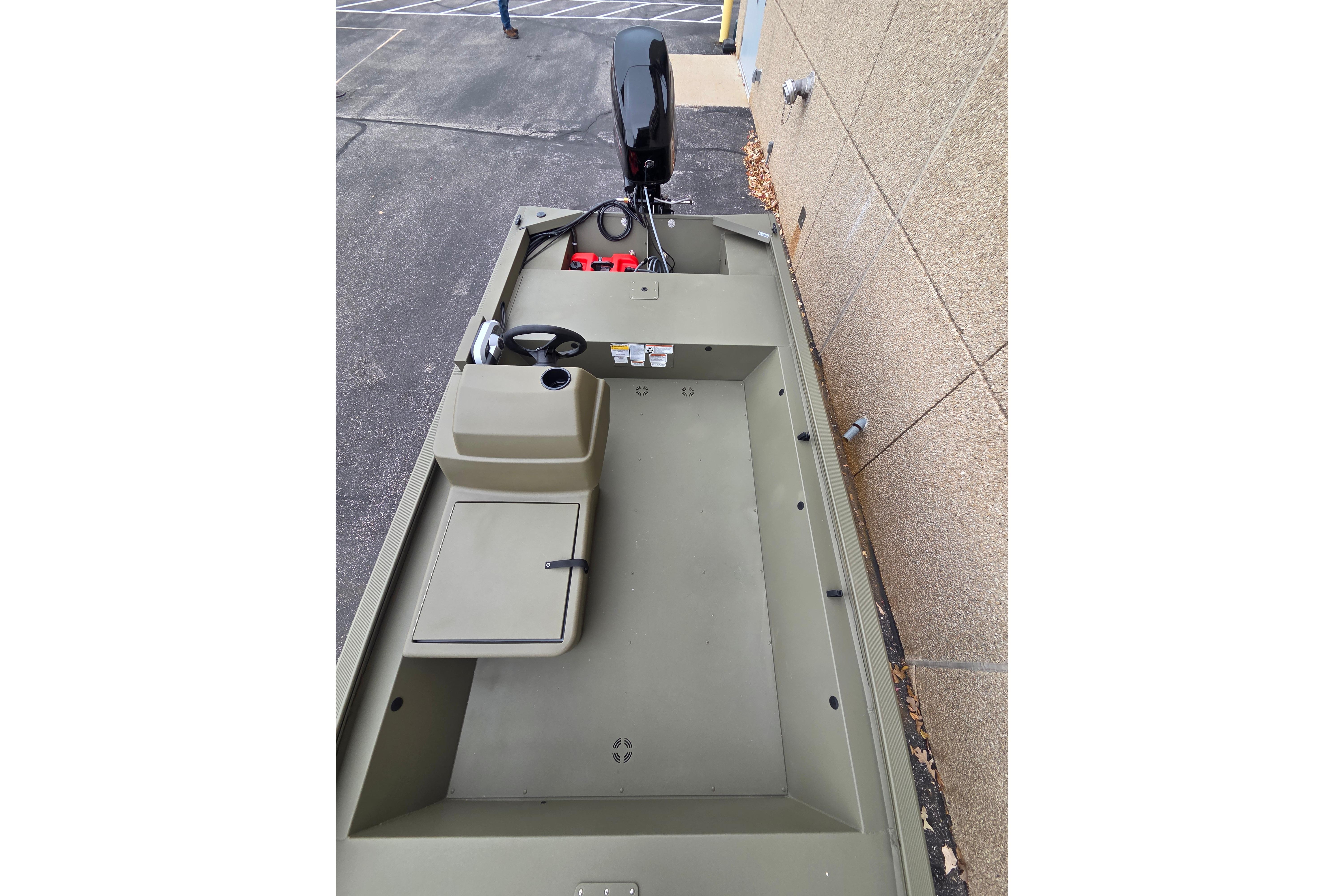 2026 Tracker Grizzly 1648 SC boat, olive green, parked beside a building.