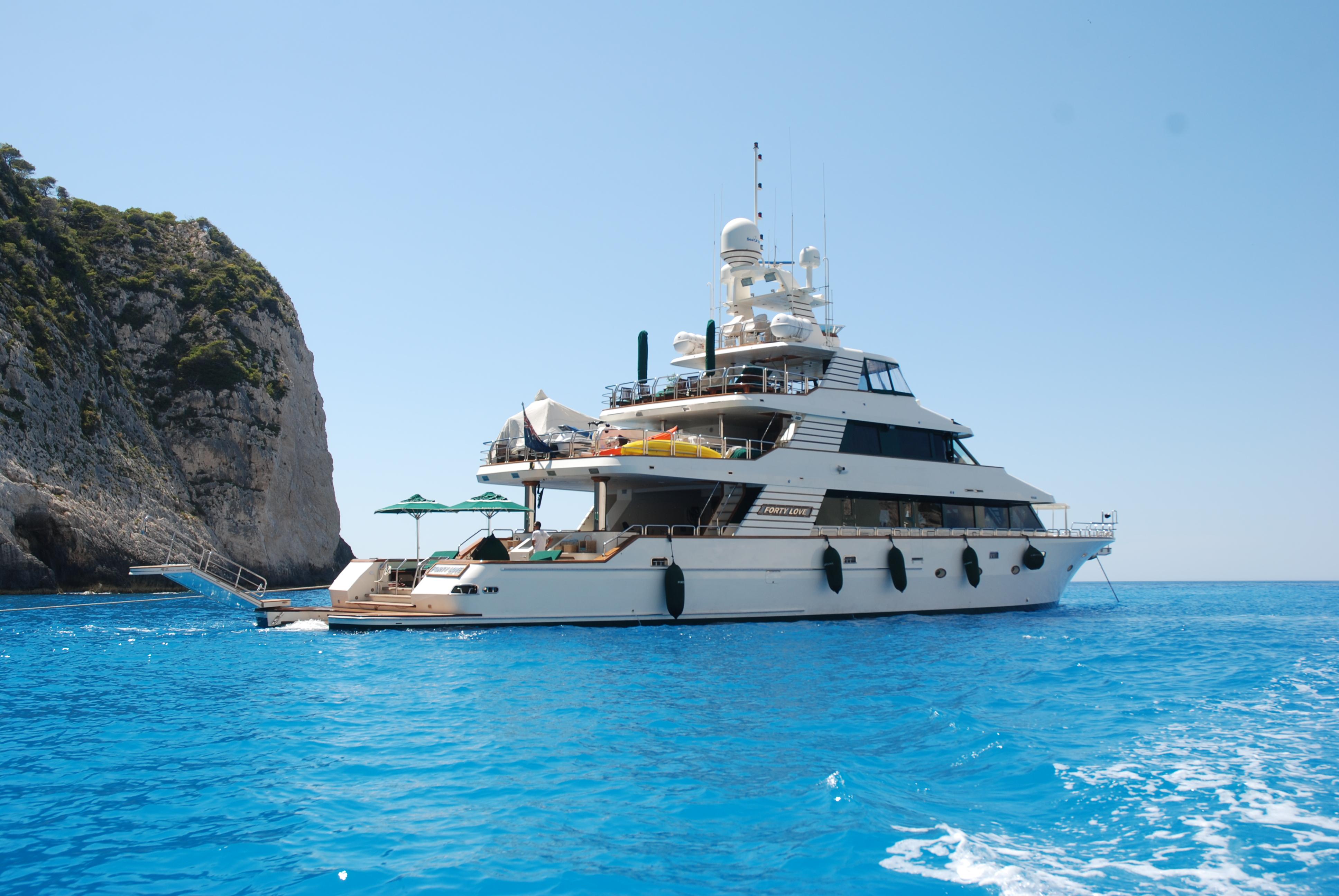 Luxurious 2004 Westport Custom yacht anchored near a rocky coastline in clear blue waters.