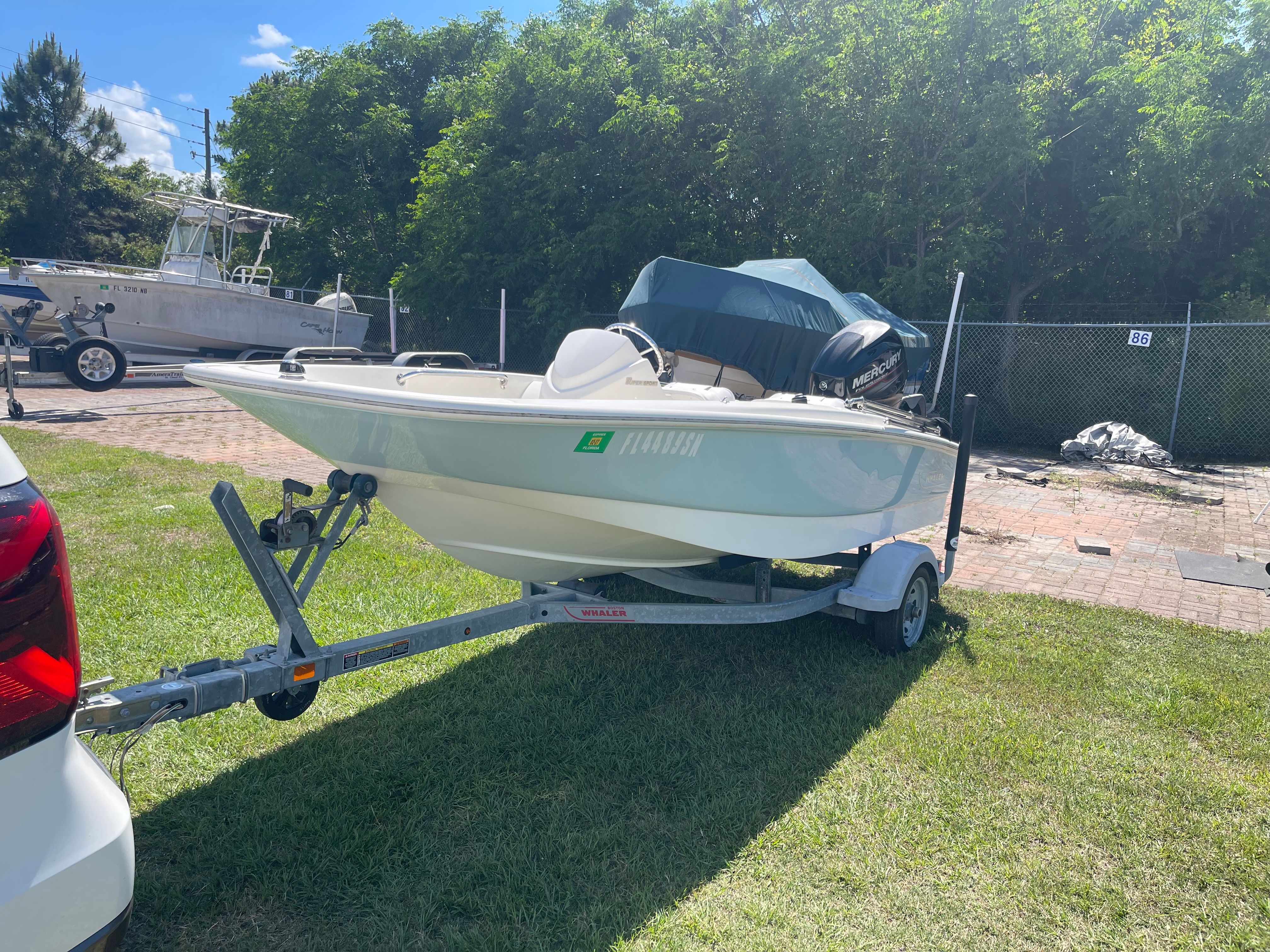 A 2017 Boston Whaler 130 Super Sport on a trailer, parked on grass.