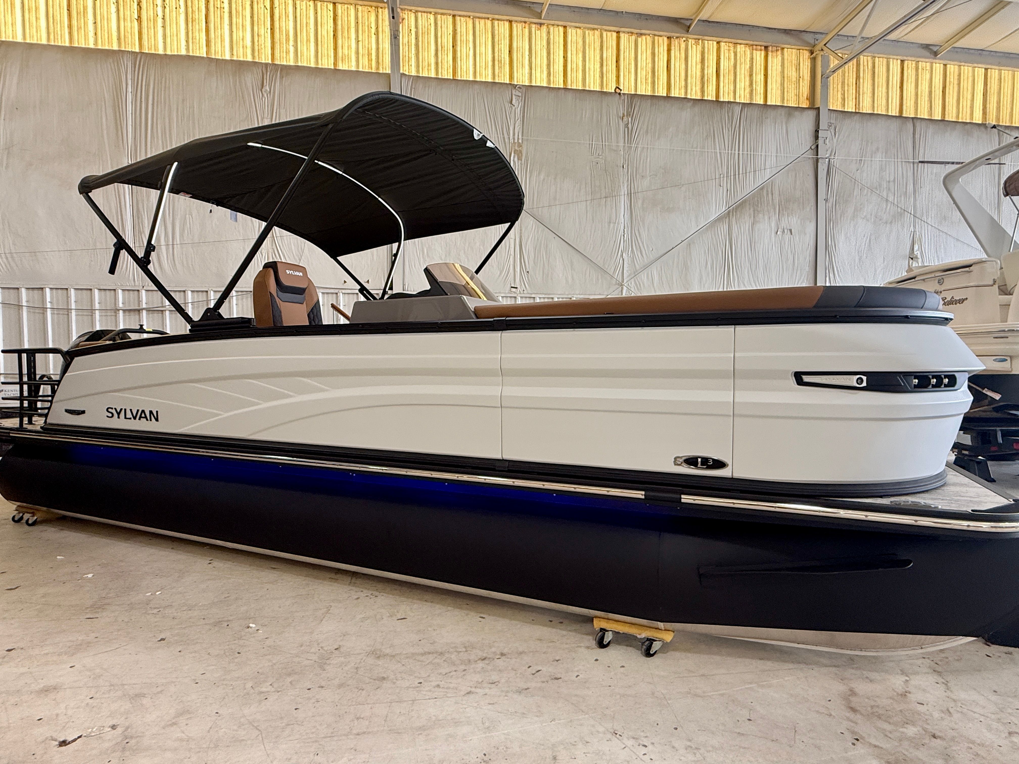 A modern pontoon boat with a black canopy and sleek lines is in a warehouse.