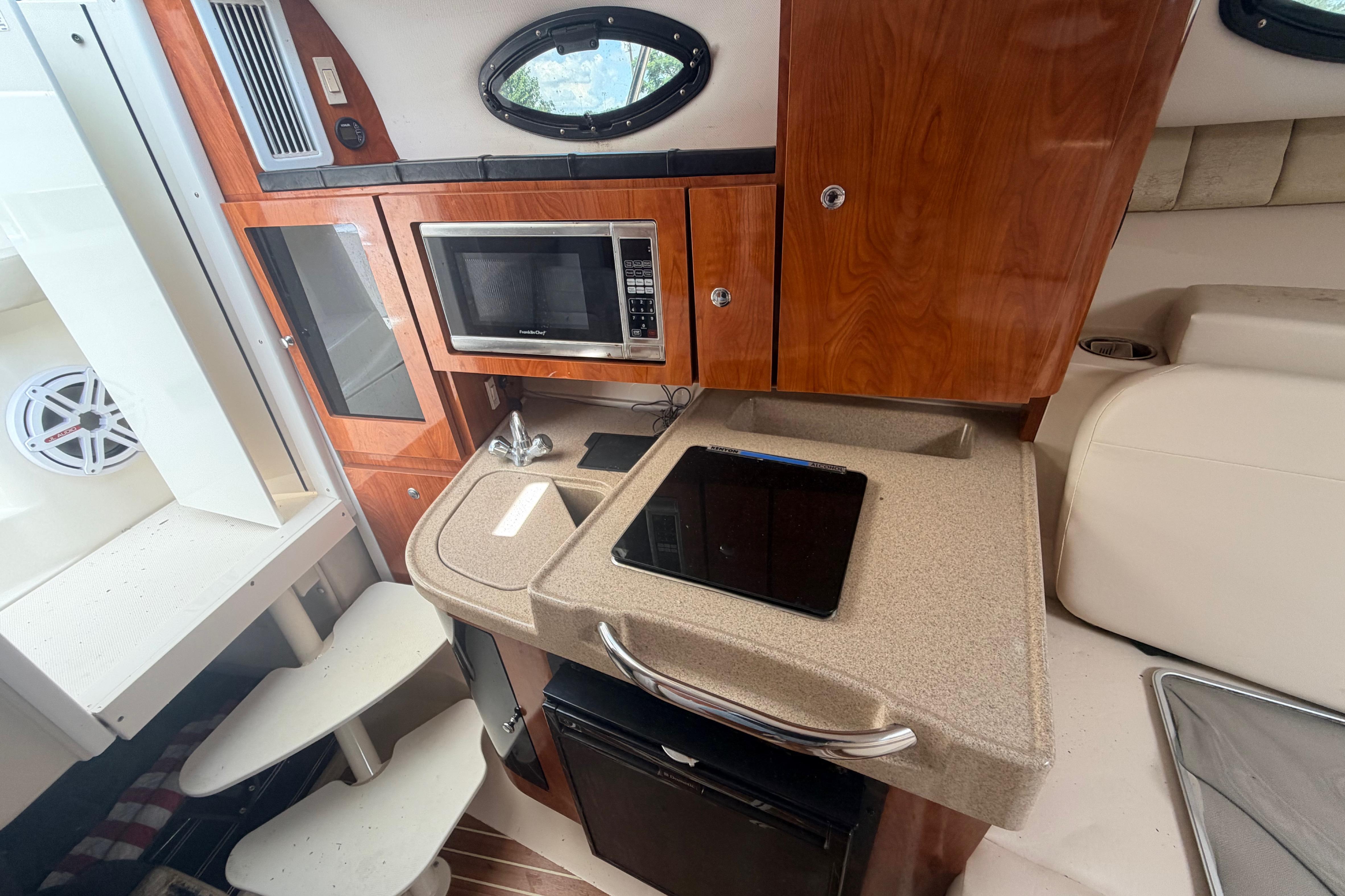 2015 Wellcraft 290 Coastal interior with kitchenette, microwave, and wooden cabinetry.