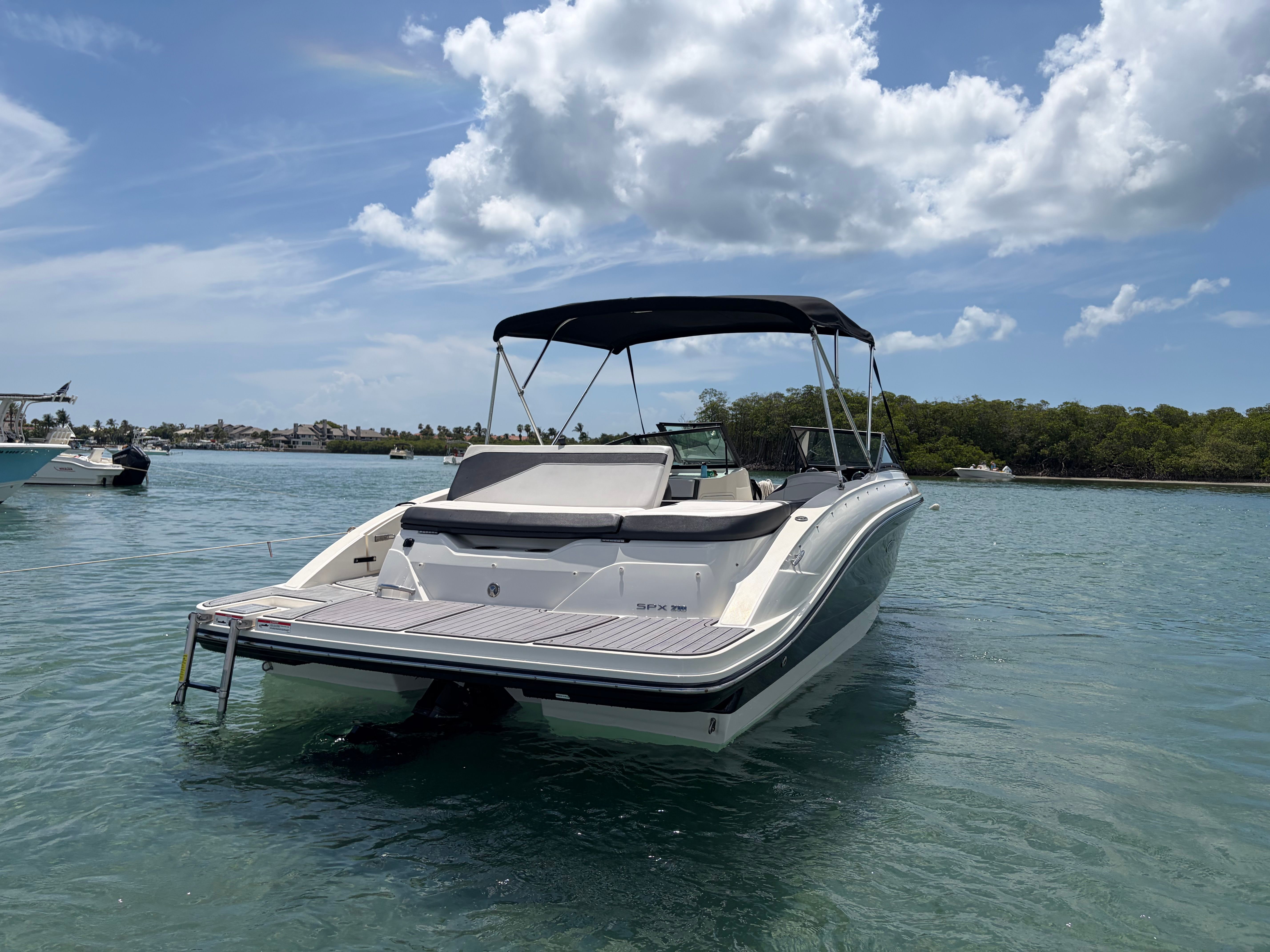 A 2018 Sea Ray SPX 210 floats on calm water under a cloudy sky.