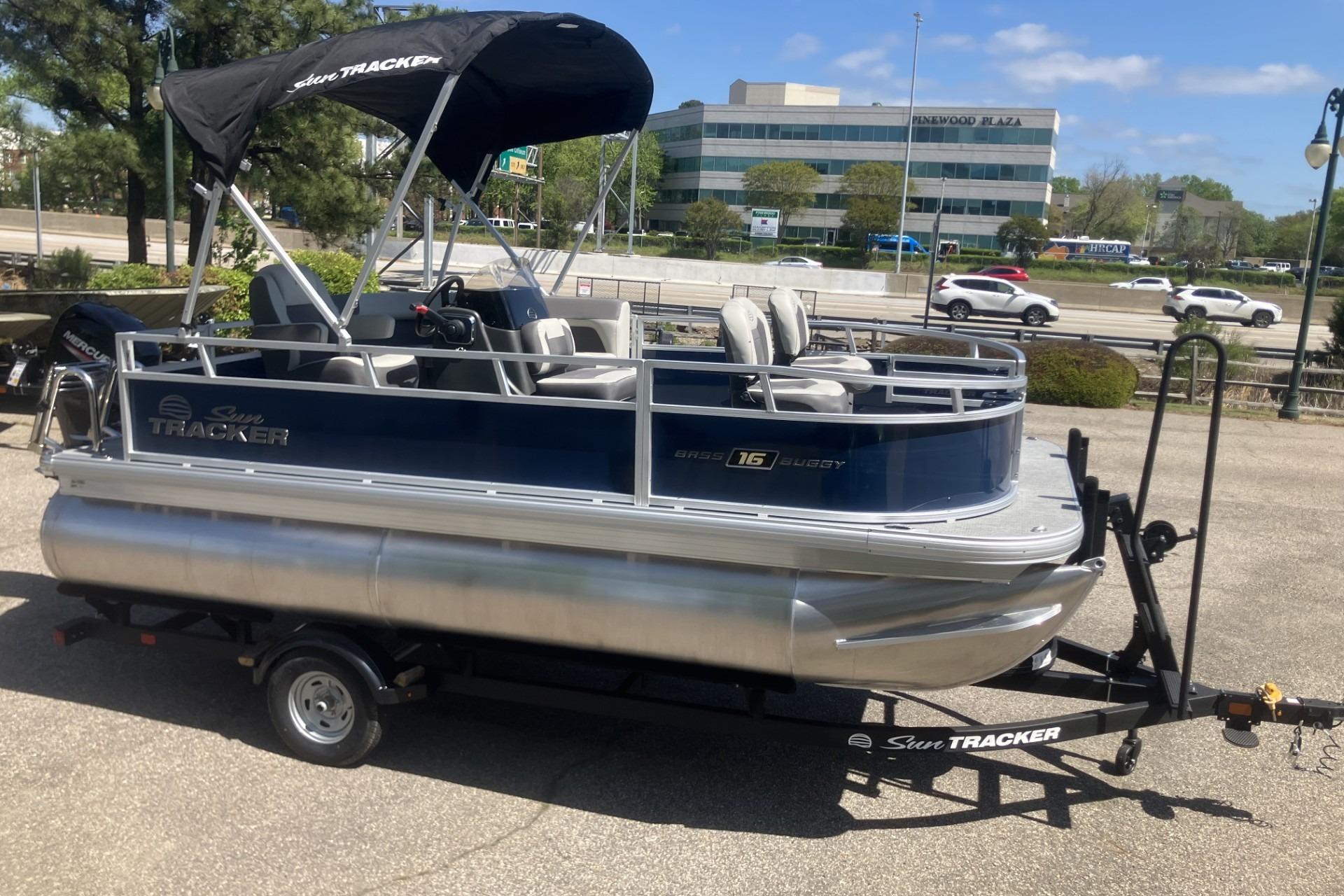 2026 Sun Tracker Bass Buggy 16 XL Select pontoon boat on trailer, parked outdoors.