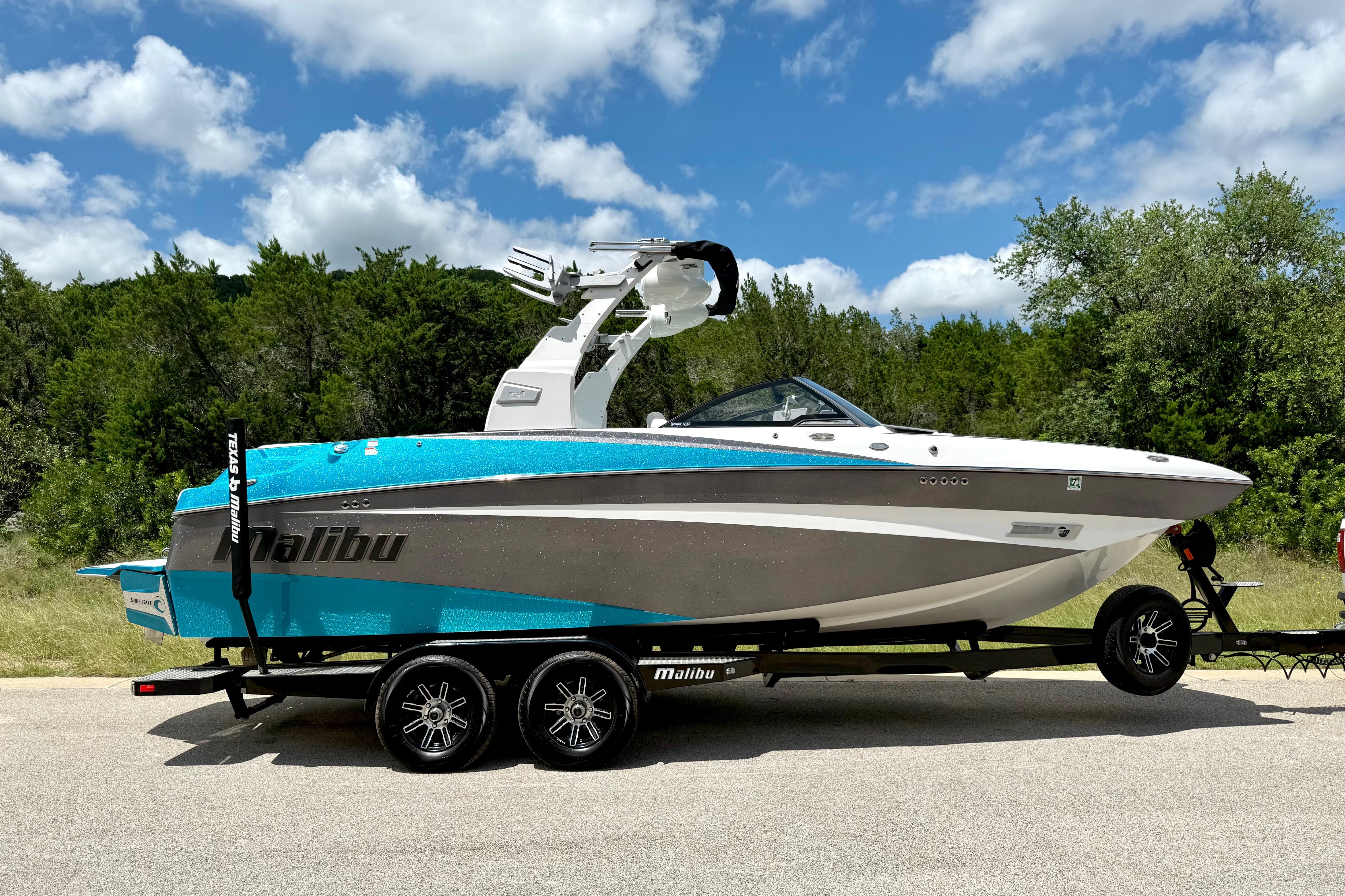 2017 Malibu M235 boat on trailer, parked on road with trees and blue sky background.