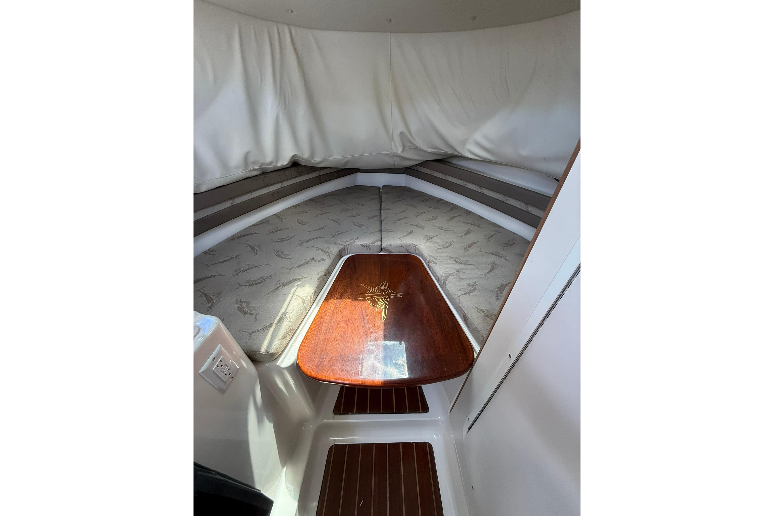 Interior cabin of 2003 Pursuit 2870 Walkaround boat with cushioned seating and wooden table.