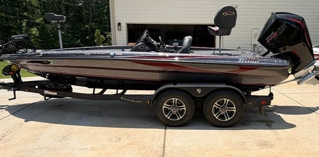 A 2024 Triton Trx19 Patriot bass boat on a trailer, parked on a driveway in front of a garage.