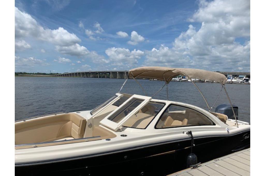 2023 Scout 240 Dorado boat docked by a scenic waterfront under a blue sky.