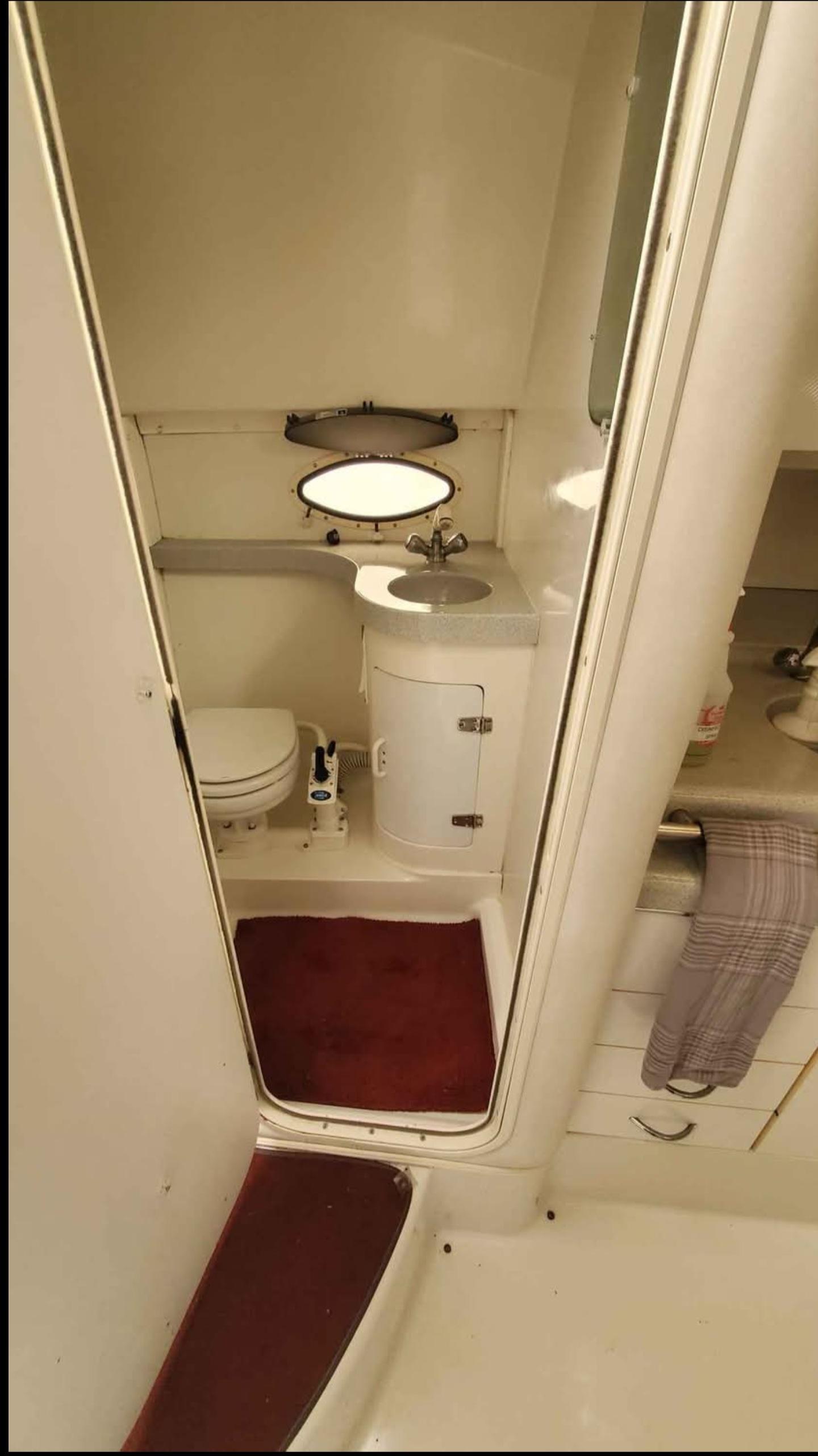 Bathroom interior of 1997 Chris-Craft 34 boat, featuring toilet, sink, and porthole window.