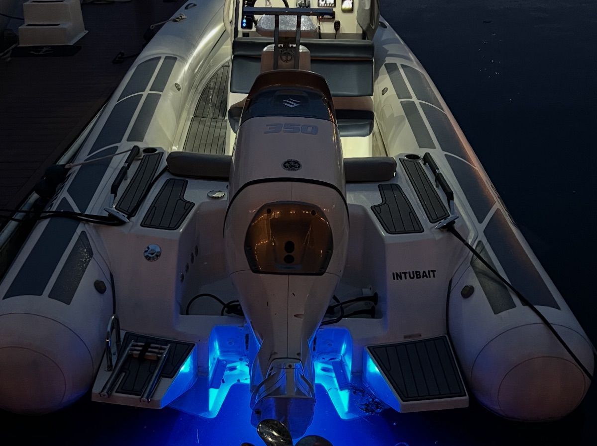 A modern inflatable boat with a powerful outboard motor and blue underwater lighting.