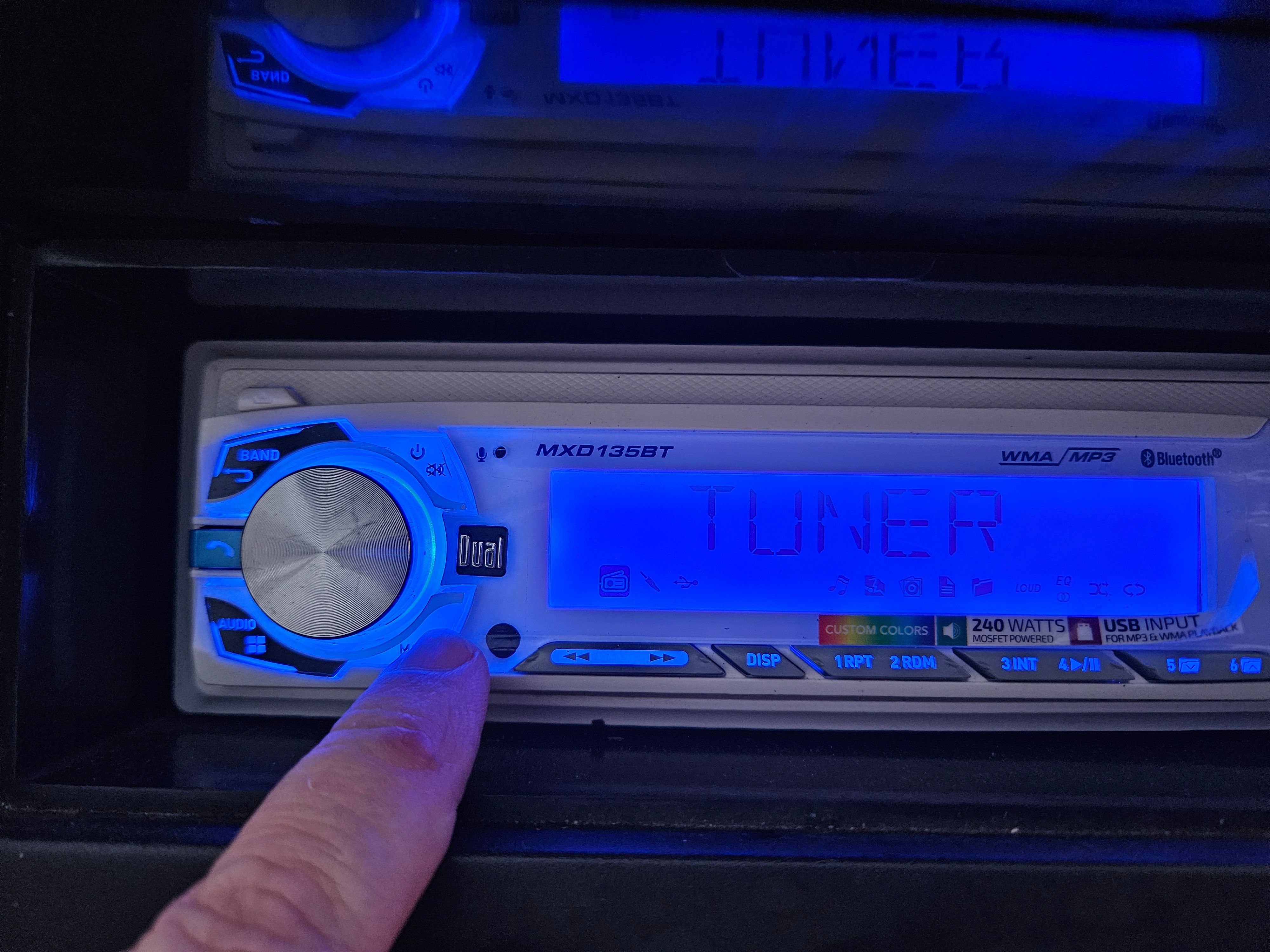 Close-up of a blue car stereo with a finger turning the volume knob.