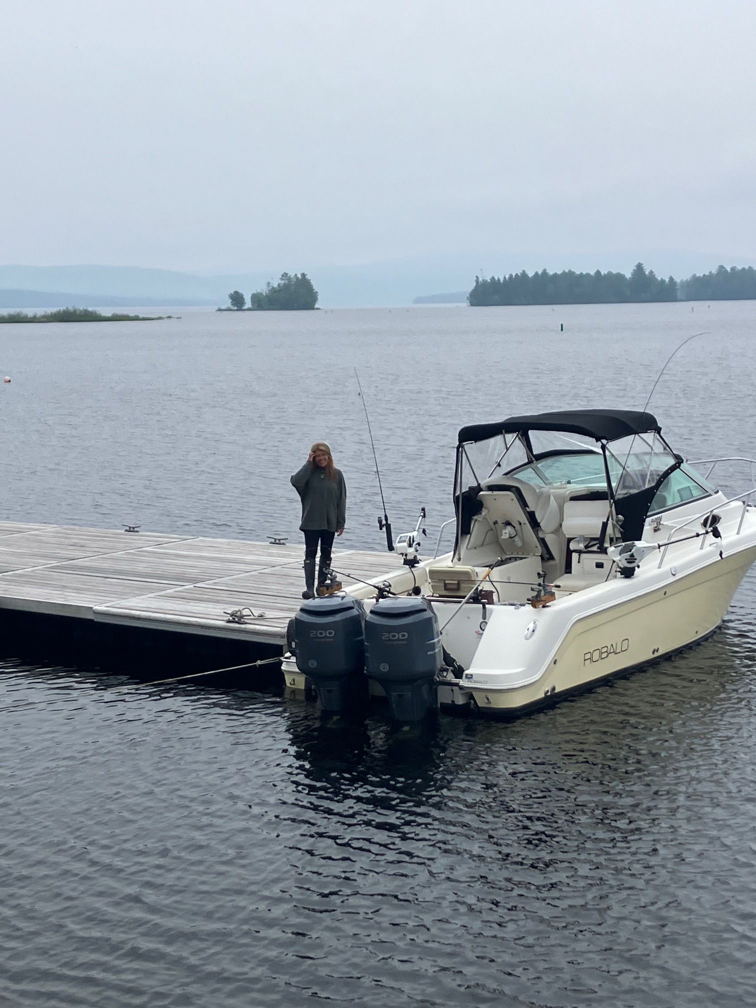 A woman stands on a dock next to a 2006 Robalo R265 Walkaround boat.