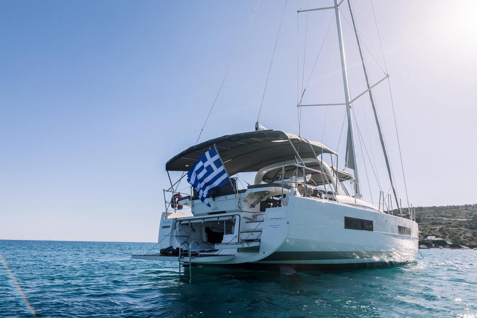 2021 Jeanneau 60 yacht sailing in clear blue waters with Greek flag.