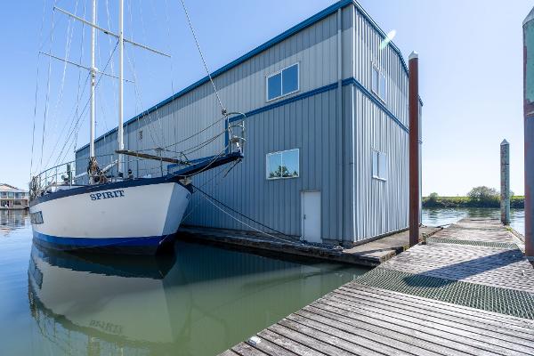 Sailboat docked beside 1985 Custom Larson Boathouse on calm water.