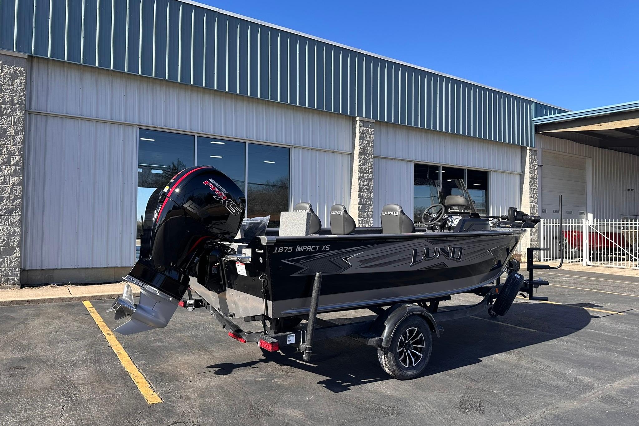 2026 Lund 1875 Impact XS SS boat parked outside a warehouse on a sunny day.