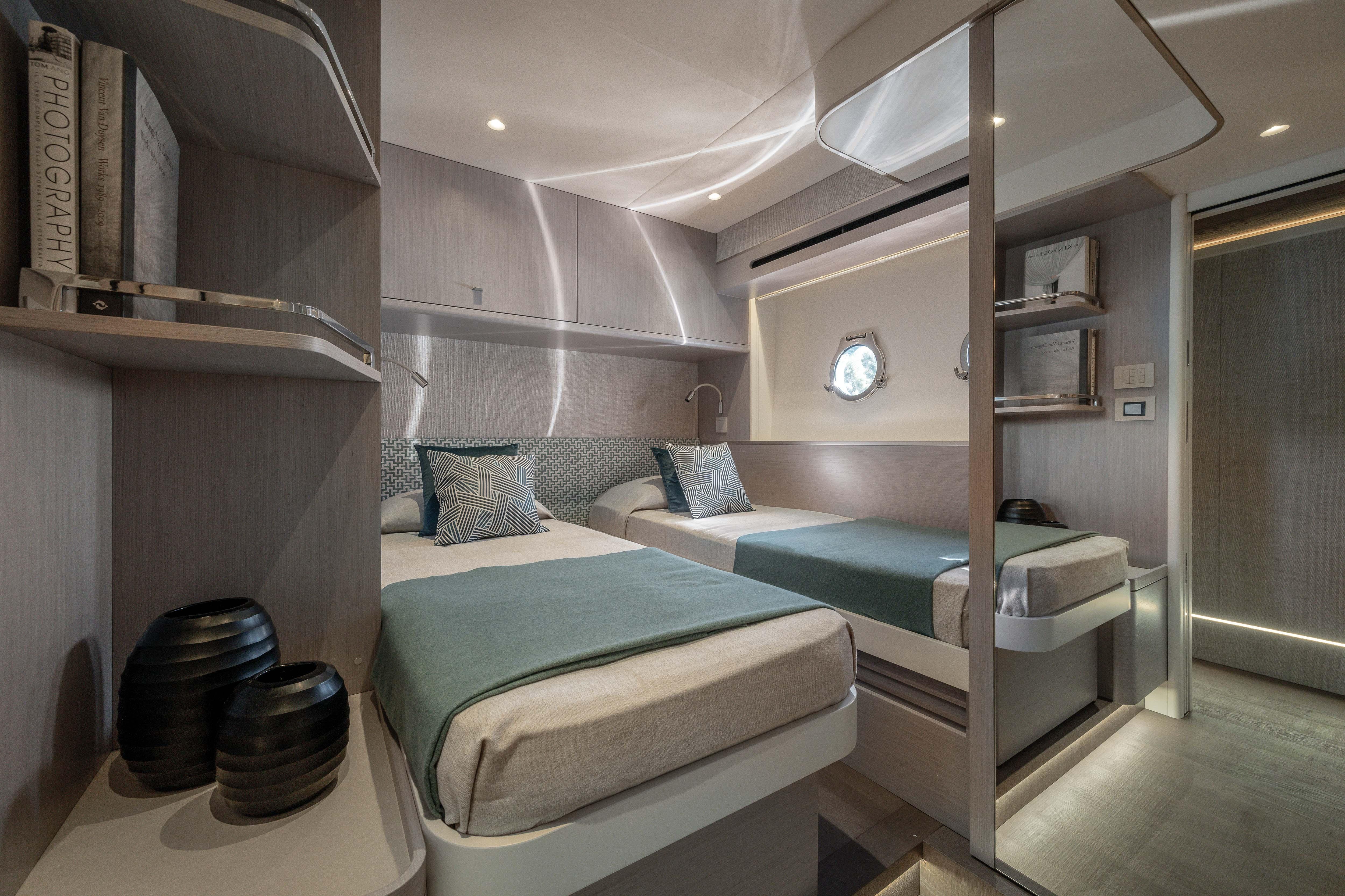 Elegant cabin interior with twin beds, modern shelving, and a porthole.