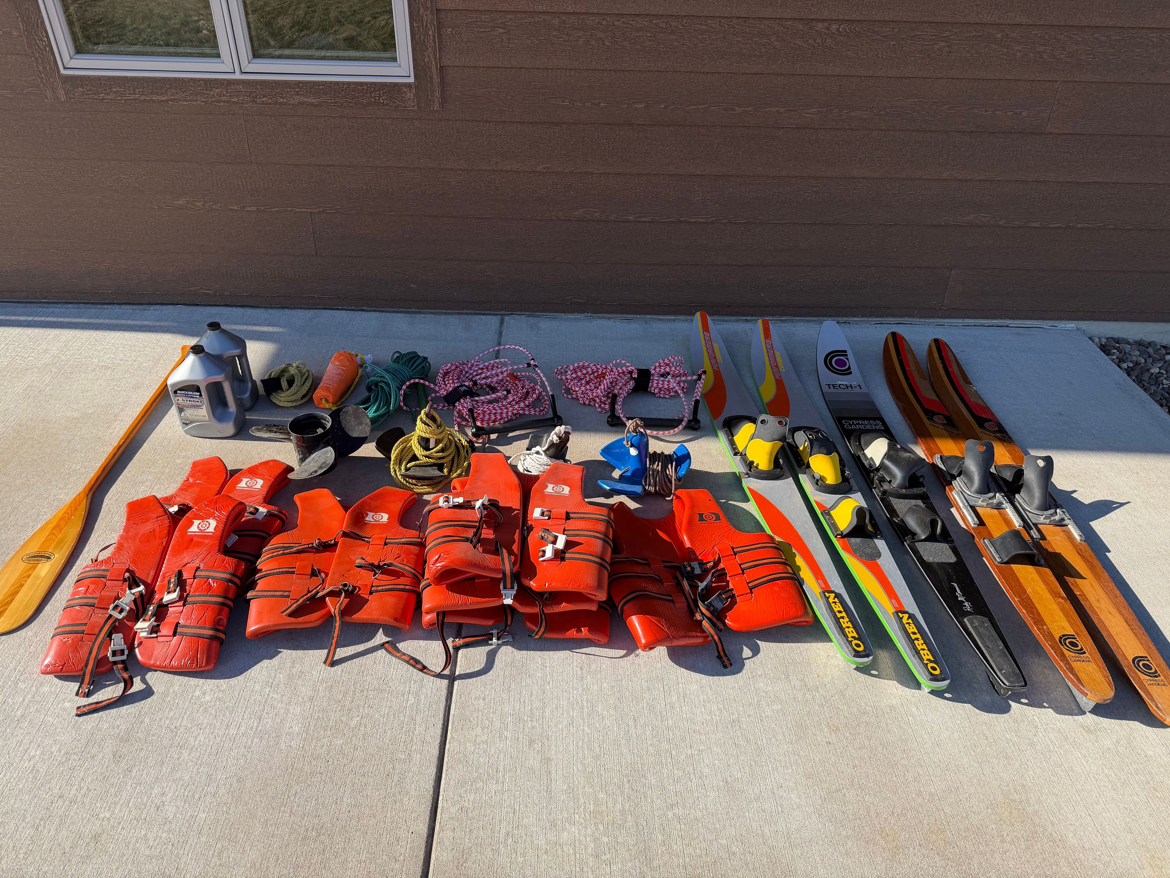 A collection of water sports gear, including life jackets, water skis, and ropes, on a concrete floor.