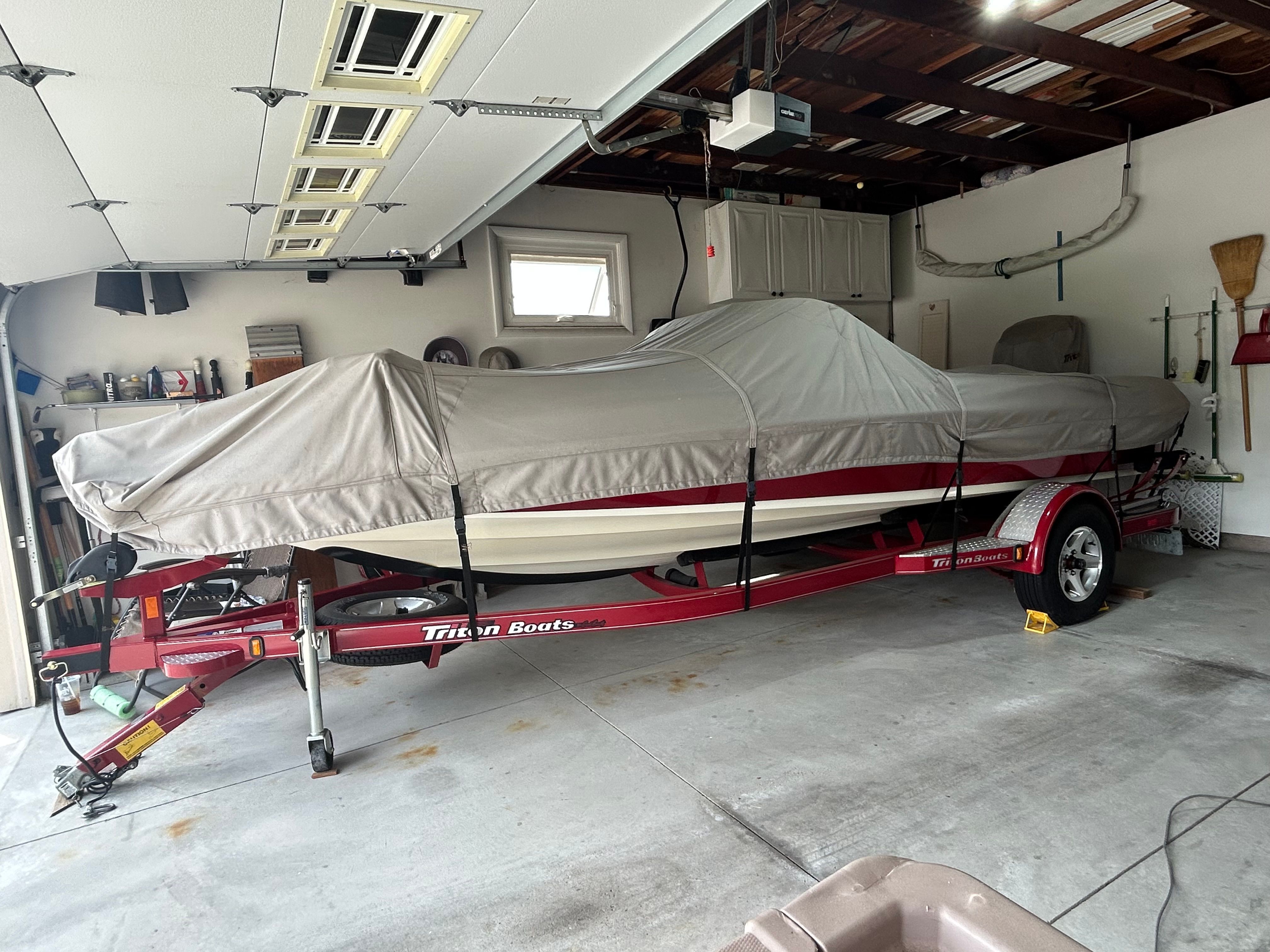 A 2003 Triton 190FS boat on a trailer in a garage, covered with a tarp.