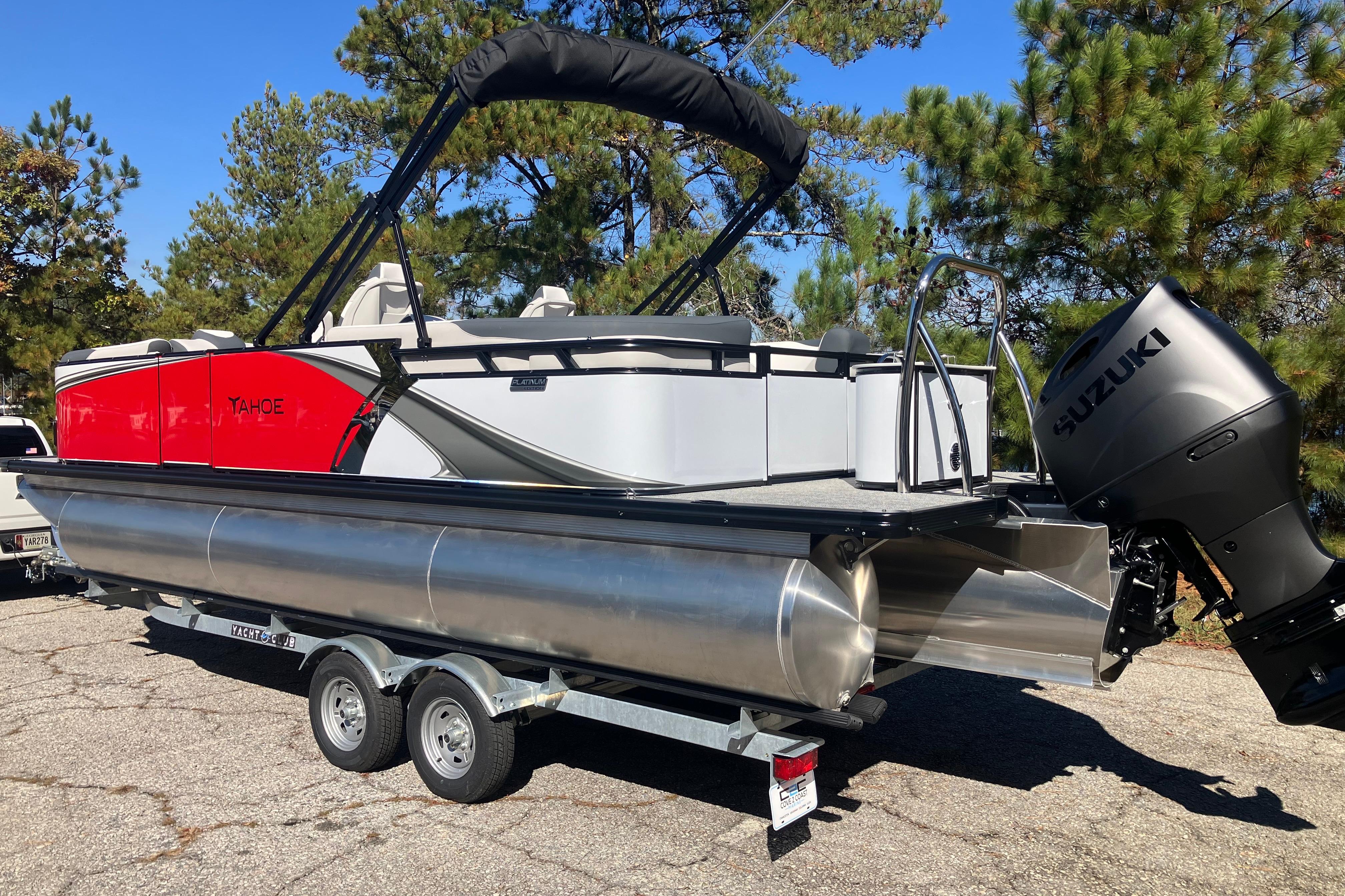 2026 Tahoe Pontoon LTZ Quad Lounger with Suzuki engine on trailer, surrounded by trees.
