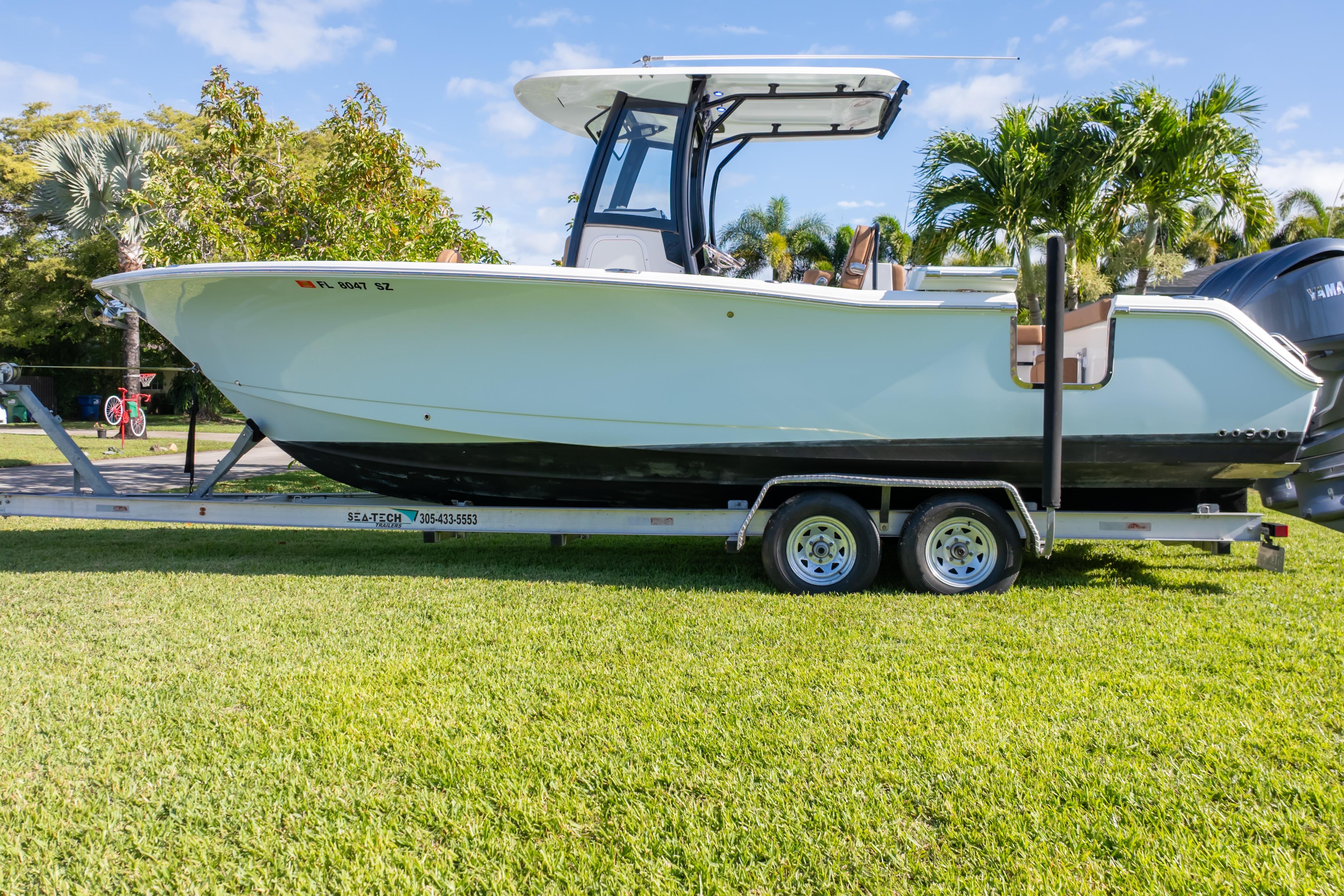 2021 Sea Hunt Gamefish 27 boat on trailer, parked on grass with palm trees.