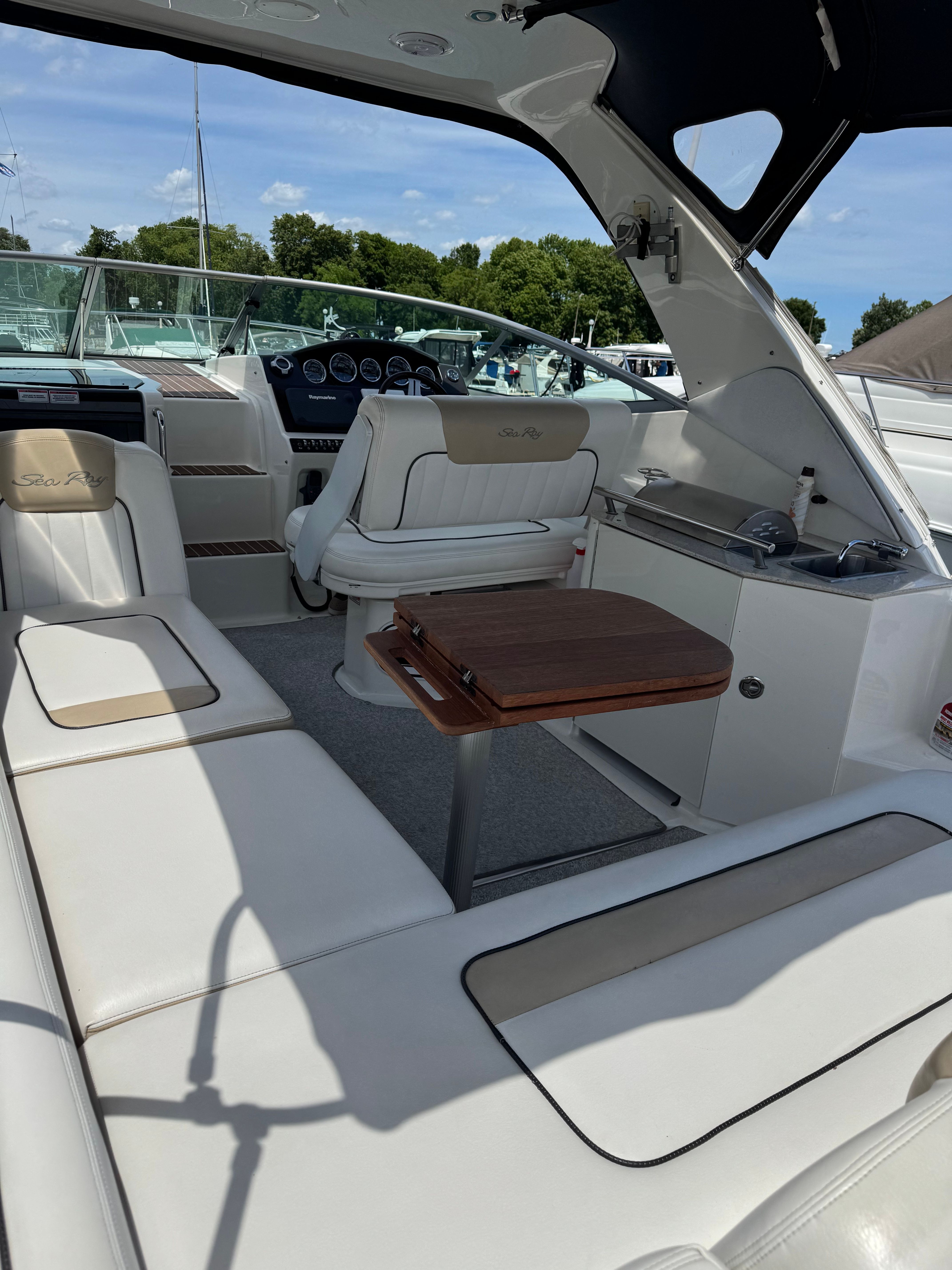 The image shows the cockpit of a 2010 Sea Ray Sundancer 310 with white seating and a wooden table.