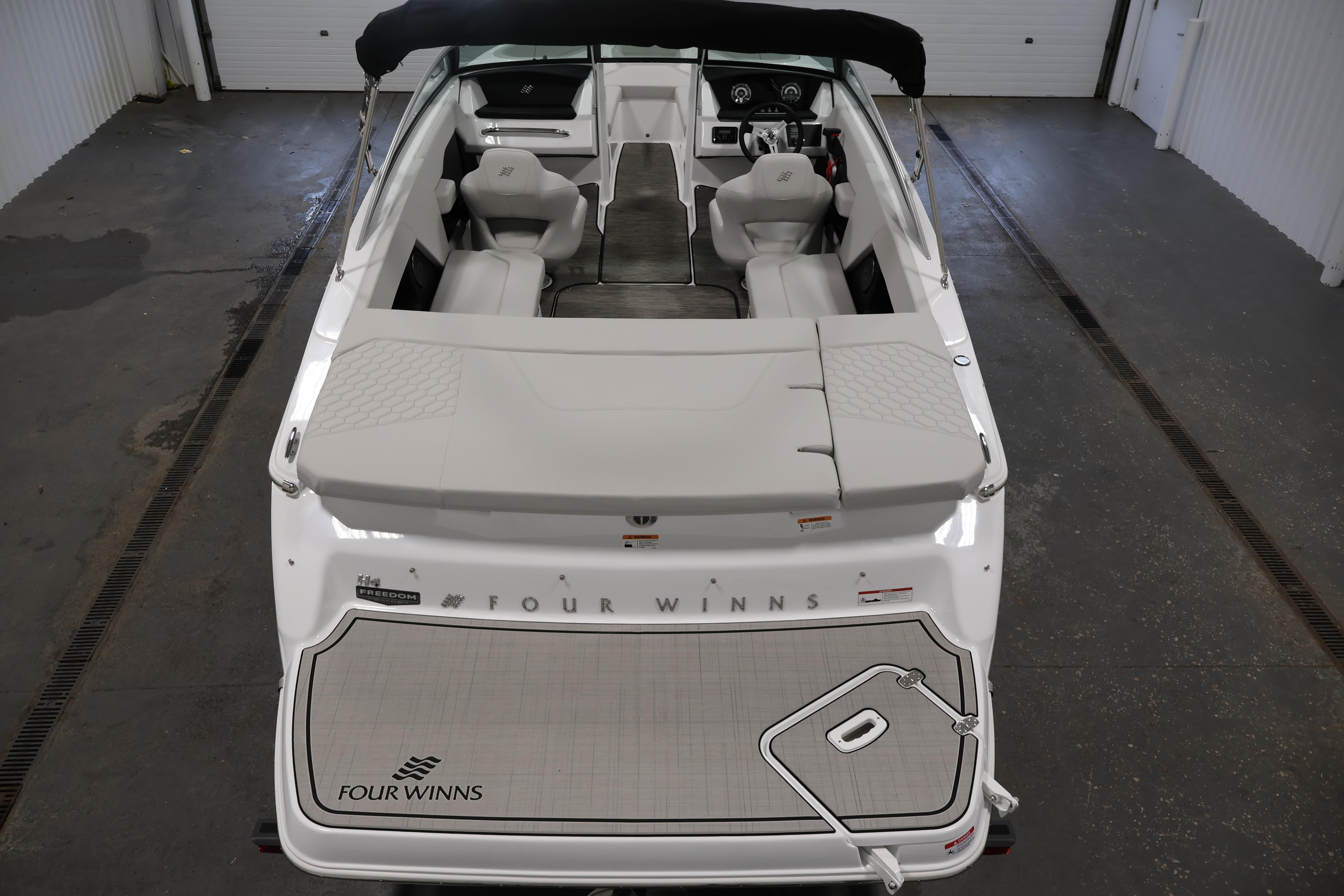 2026 Four Winns H4 Freedom boat interior, showcasing seating and dashboard in a garage setting.