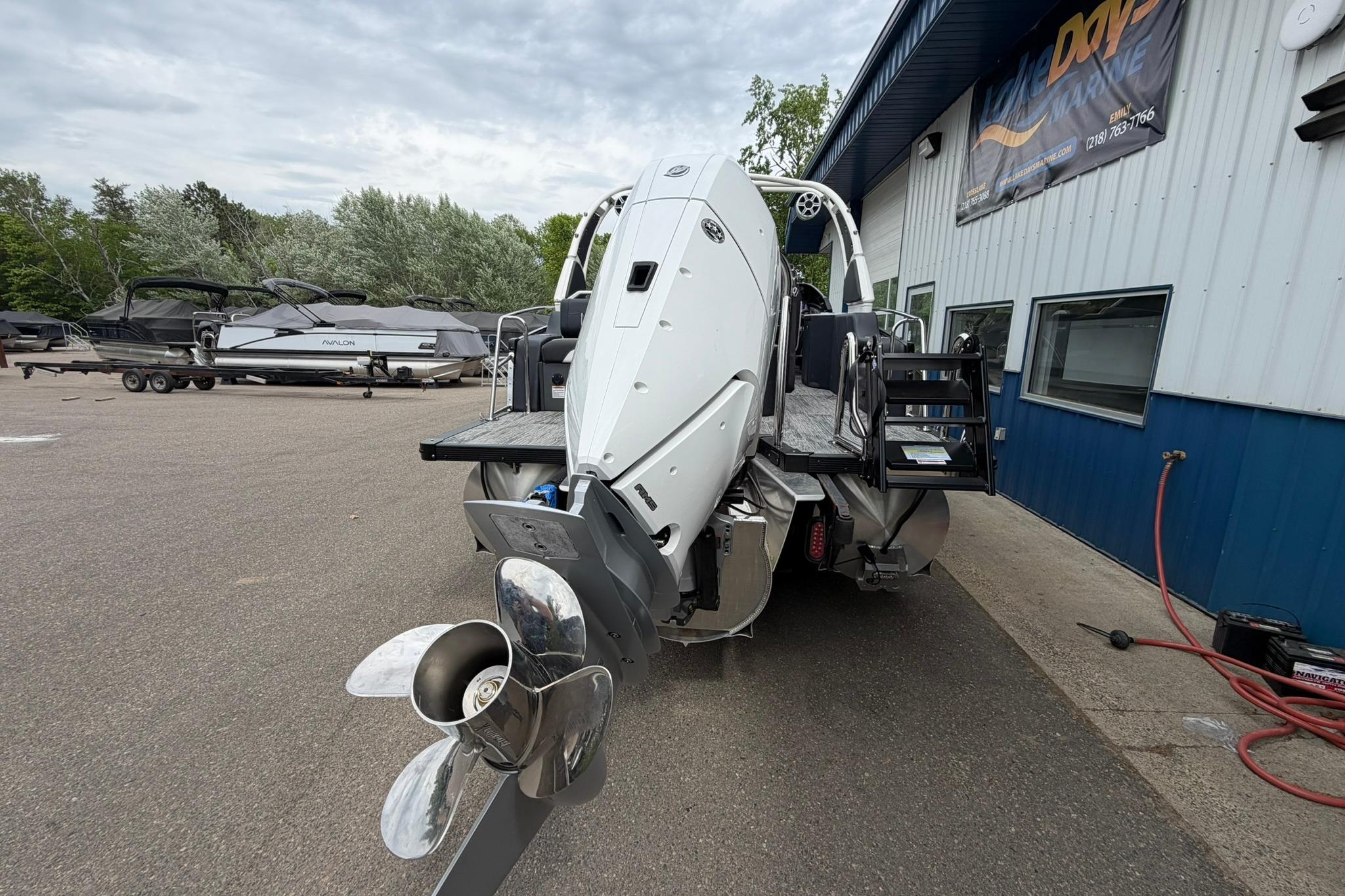 2026 Avalon Excalibur LTD Flex Lounge boat with outboard motor, parked near a blue building.