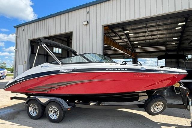 2014 Yamaha Boats 212X in red, parked on a trailer outside a warehouse.