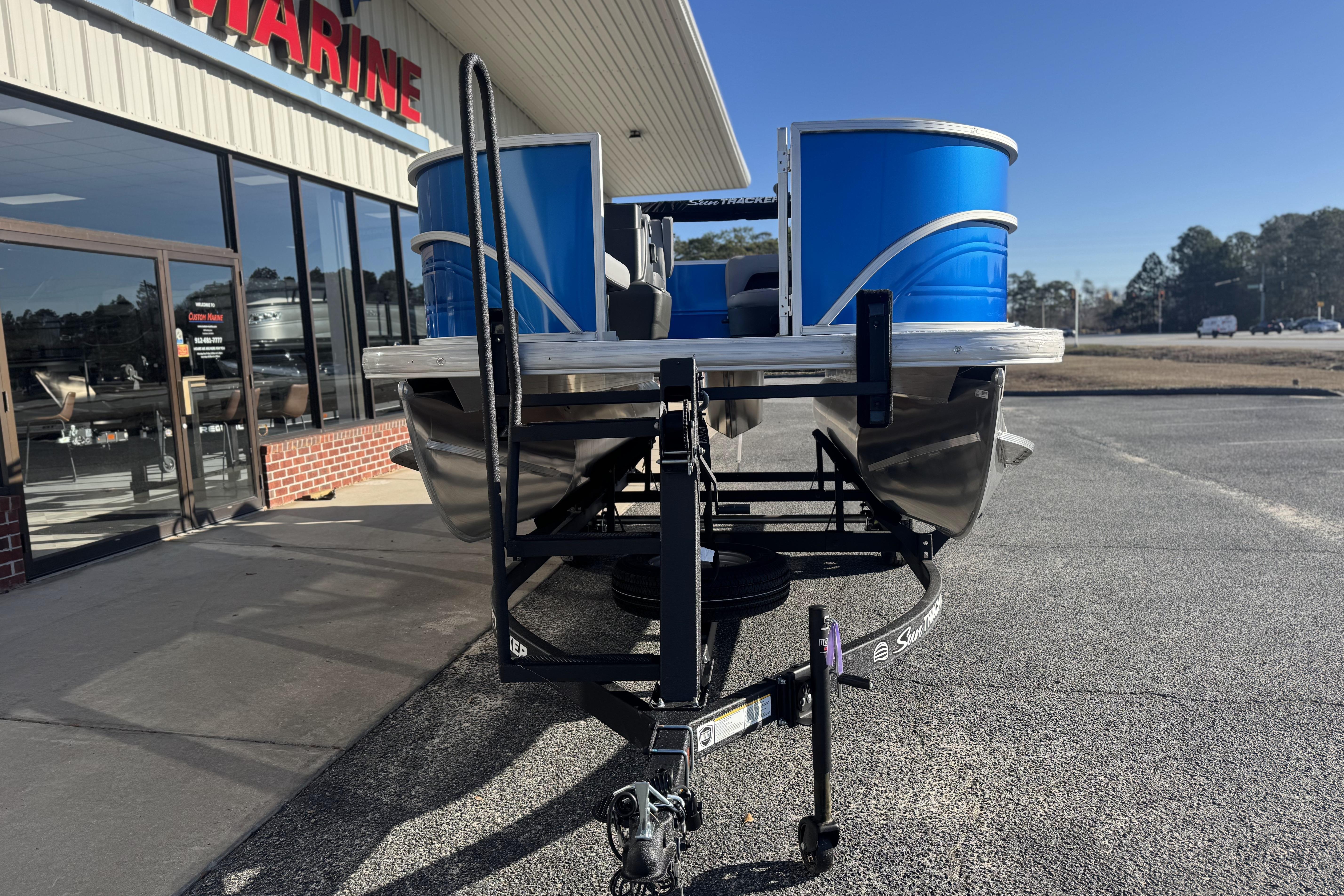 2026 Sun Tracker Party Barge 16 DLX pontoon boat on trailer outside marine store.