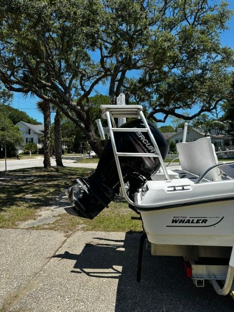 A 2008 Boston Whaler 200 Dauntless with an outboard motor, parked on a trailer under trees.