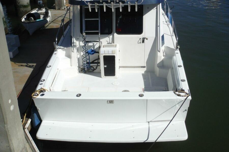 1990 Mediterranean Sport Fish boat docked, rear view showing spacious deck and fishing equipment.