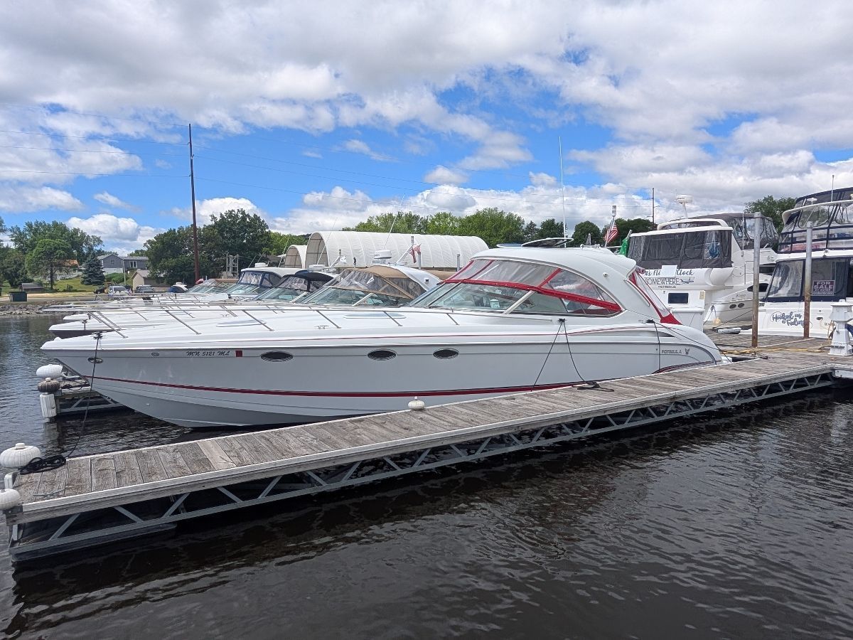 A white motor yacht is docked. The sky is cloudy, and trees are visible in the background.