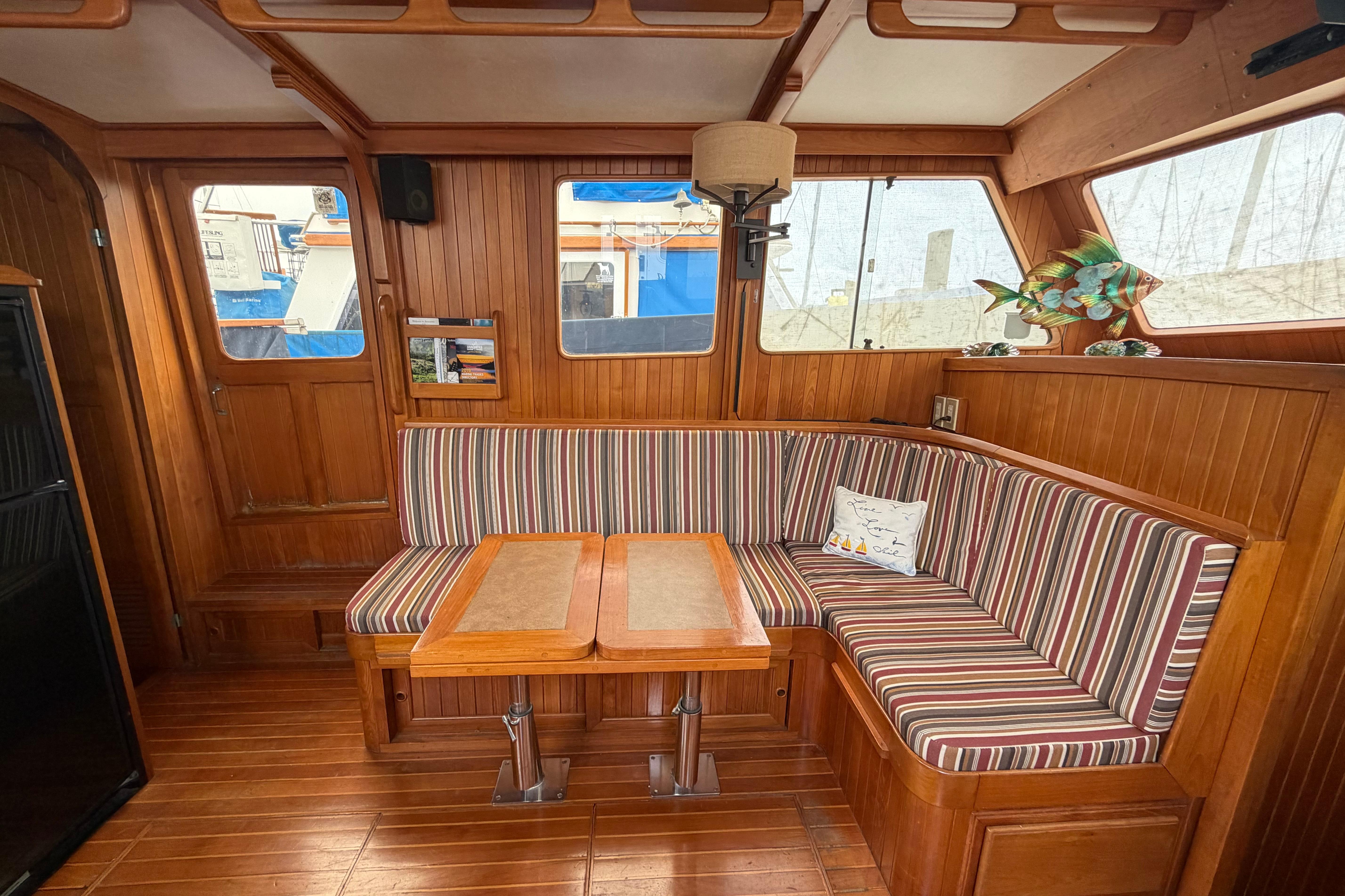 1988 Monk 36 yacht interior with striped seating, wooden table, and nautical decor.