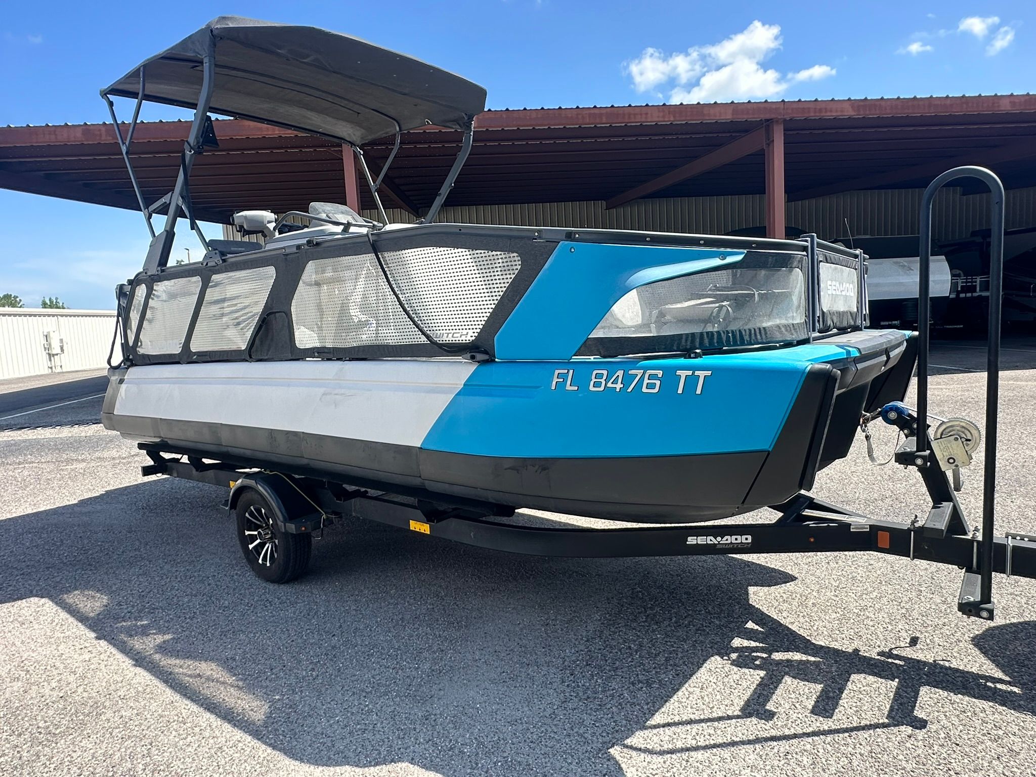 A 2023 Sea-Doo 21 SWITCH SPORT on a trailer, featuring a blue and gray hull, under a shelter.