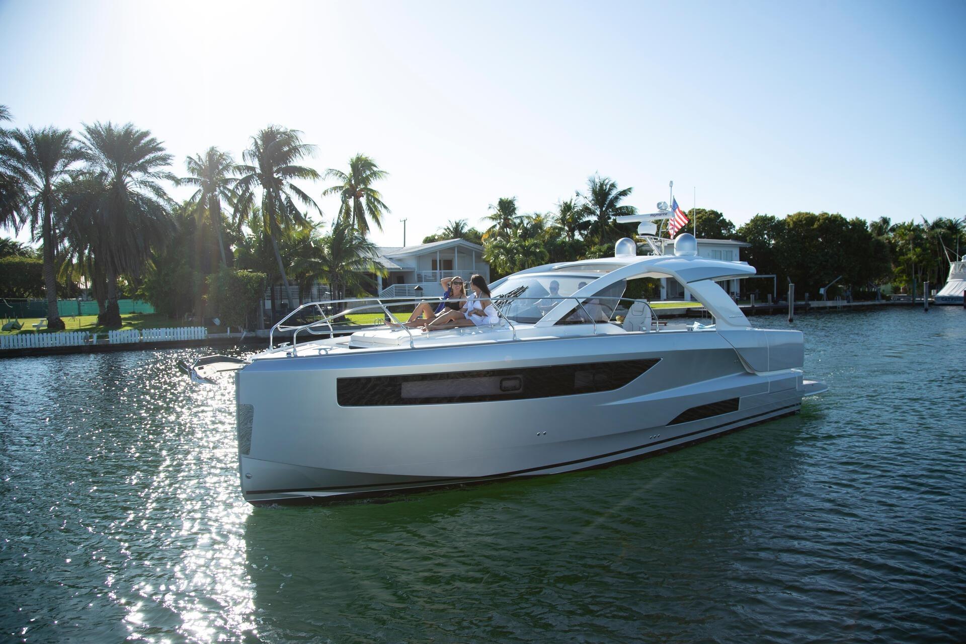 2027 Jeanneau DB/43 OB yacht cruising on a sunny day near palm-lined shore.
