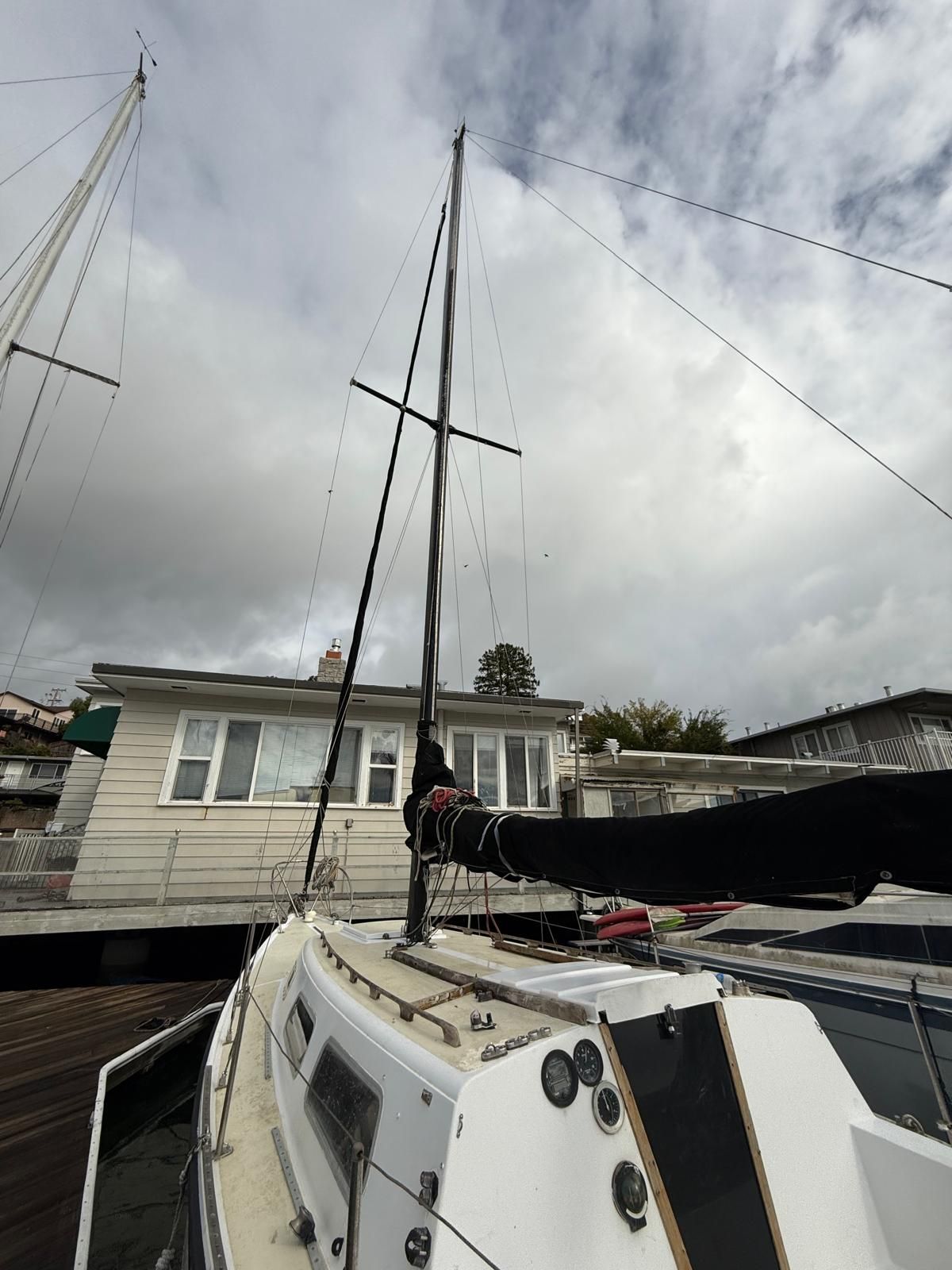 A sailboat docked at a harbor, featuring a tall mast and cloudy sky in the background.