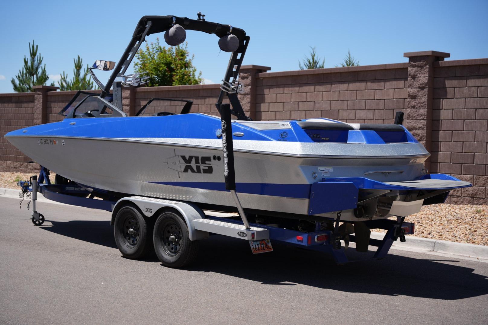 2015 Axis A24 boat on trailer, blue and silver, parked by brick wall.