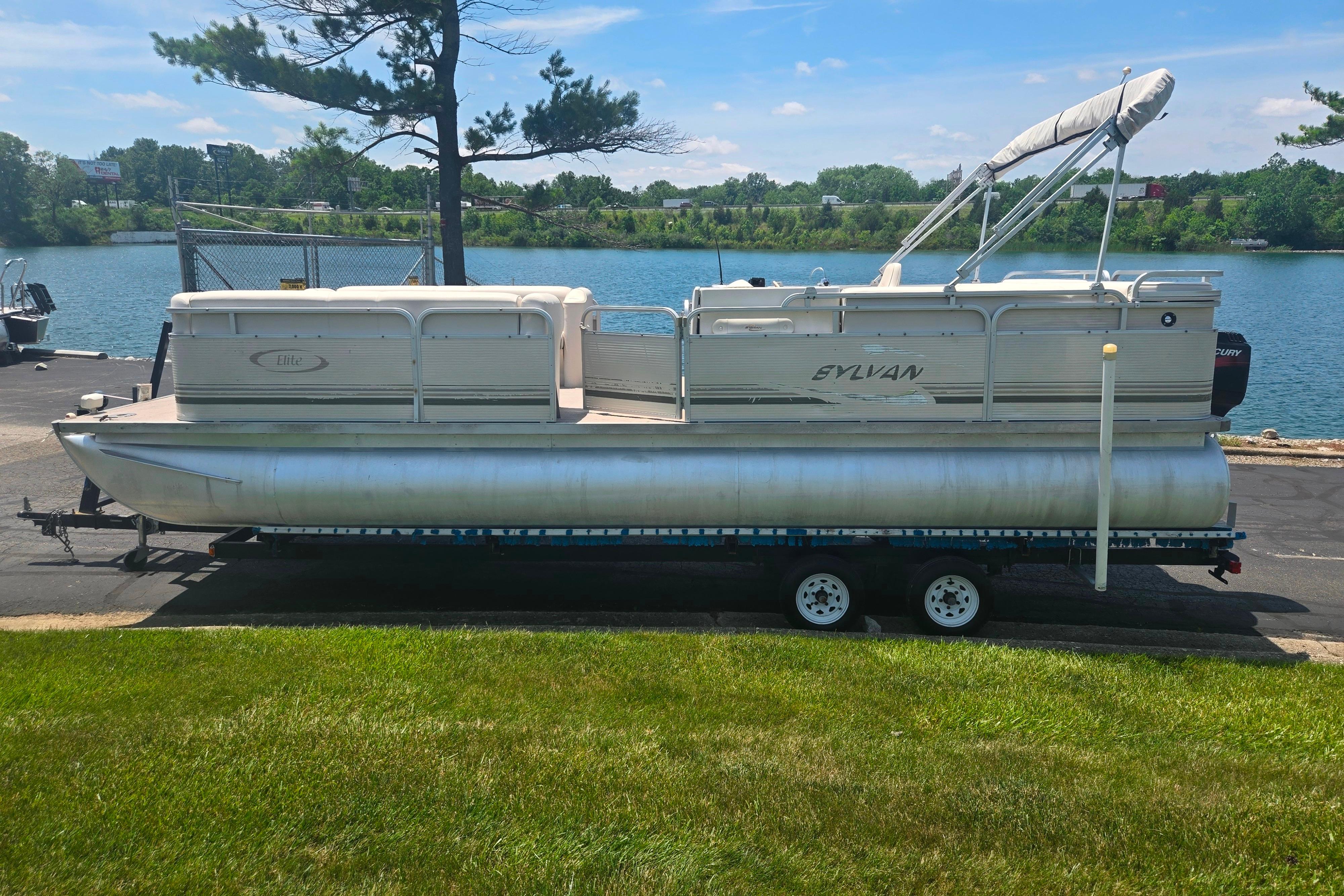 2000 Sylvan 824 Elite Cruise pontoon boat on trailer by a lake.